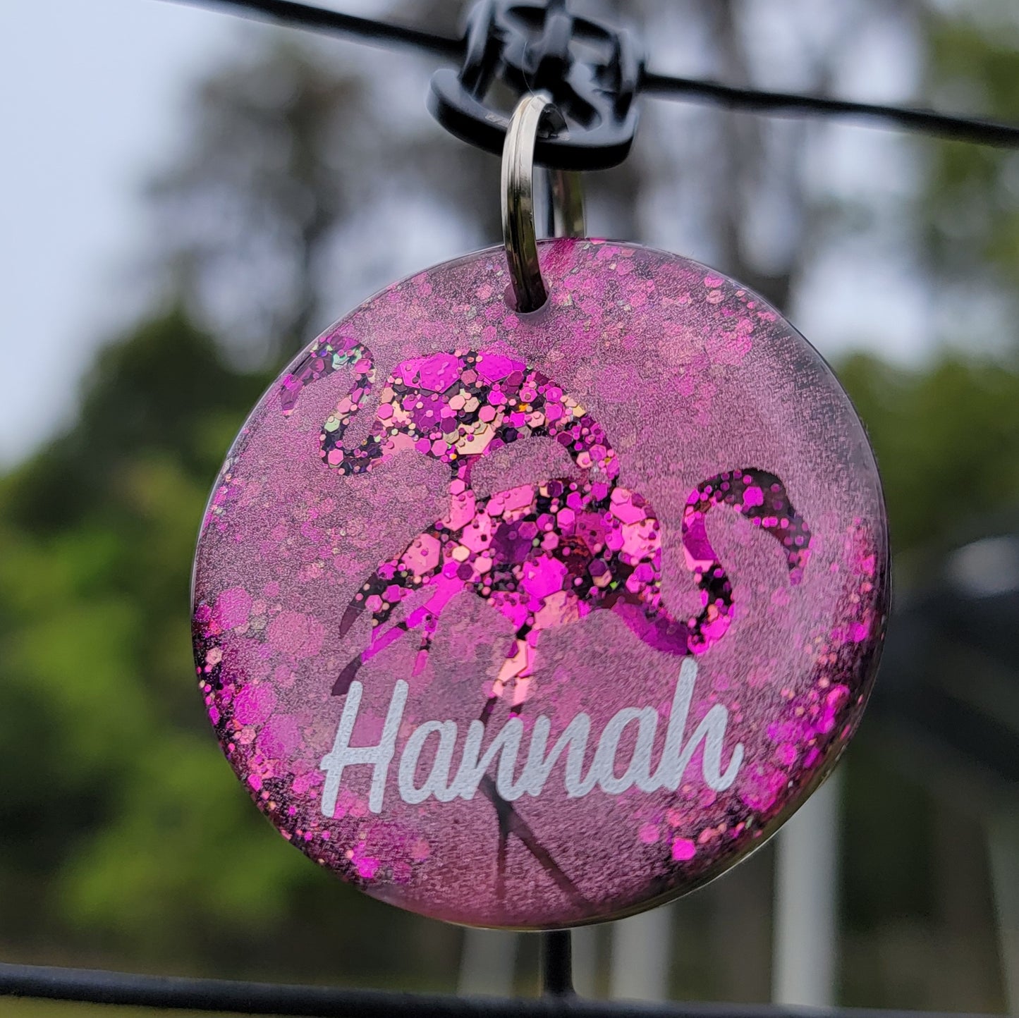 Round epoxy resin piece, hot pink glitter with metallic flamingo design shown with personalization in silver vinyl.