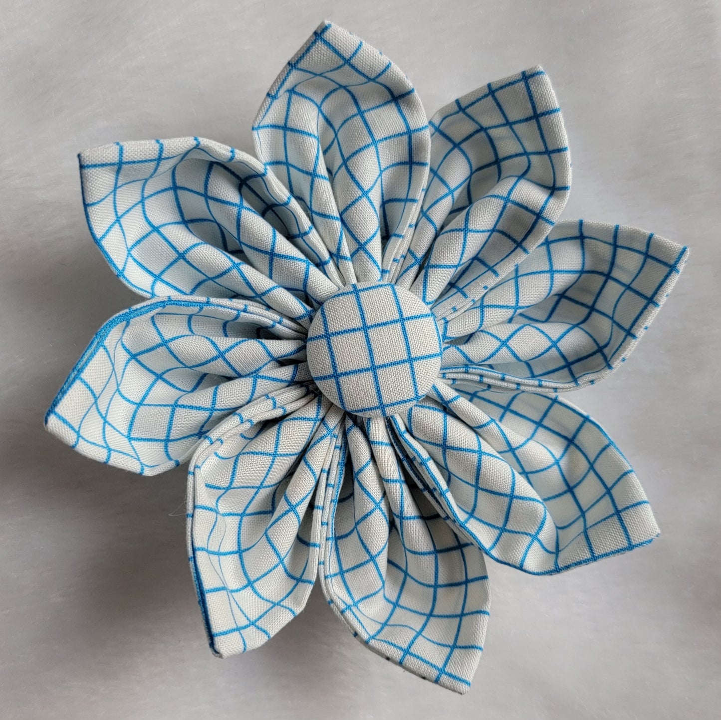 Fabric flower with eight petals and fabric covered button center, print is blue and white plaid.