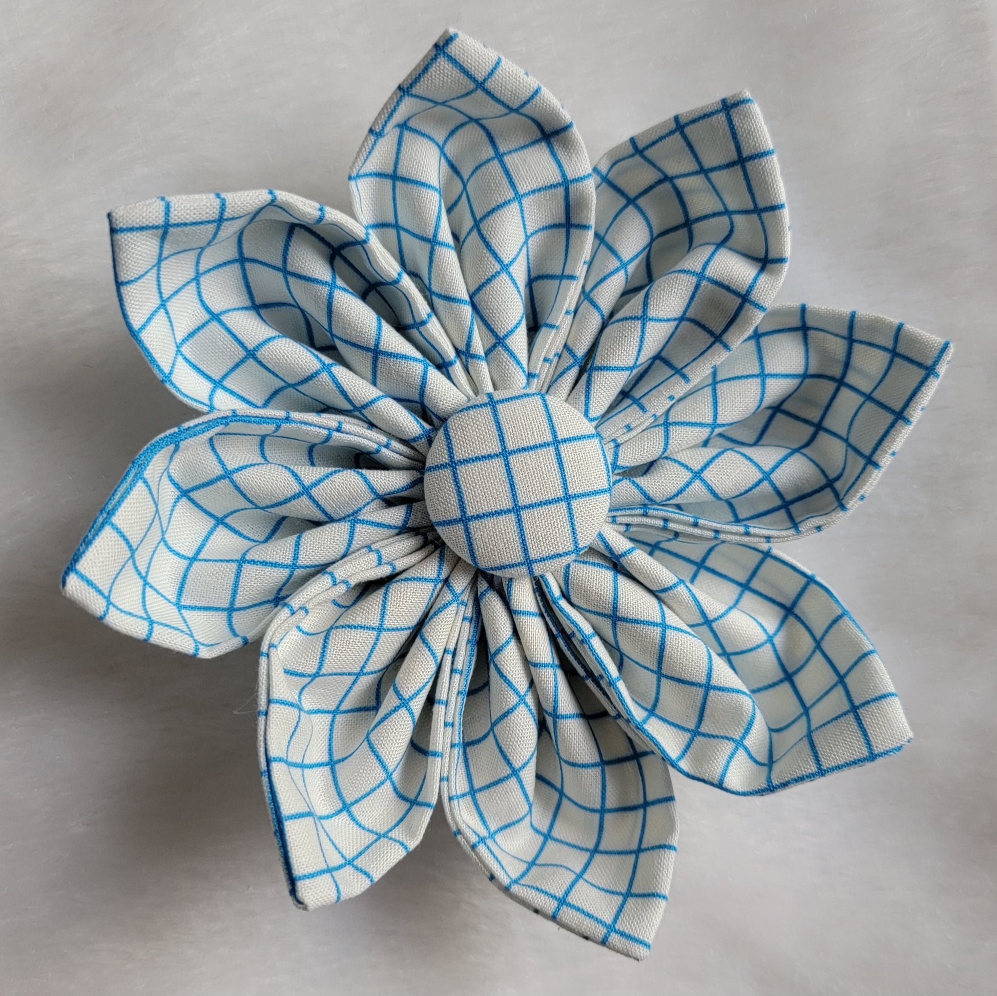 Fabric flower with eight petals and fabric covered button center, print is blue and white plaid.