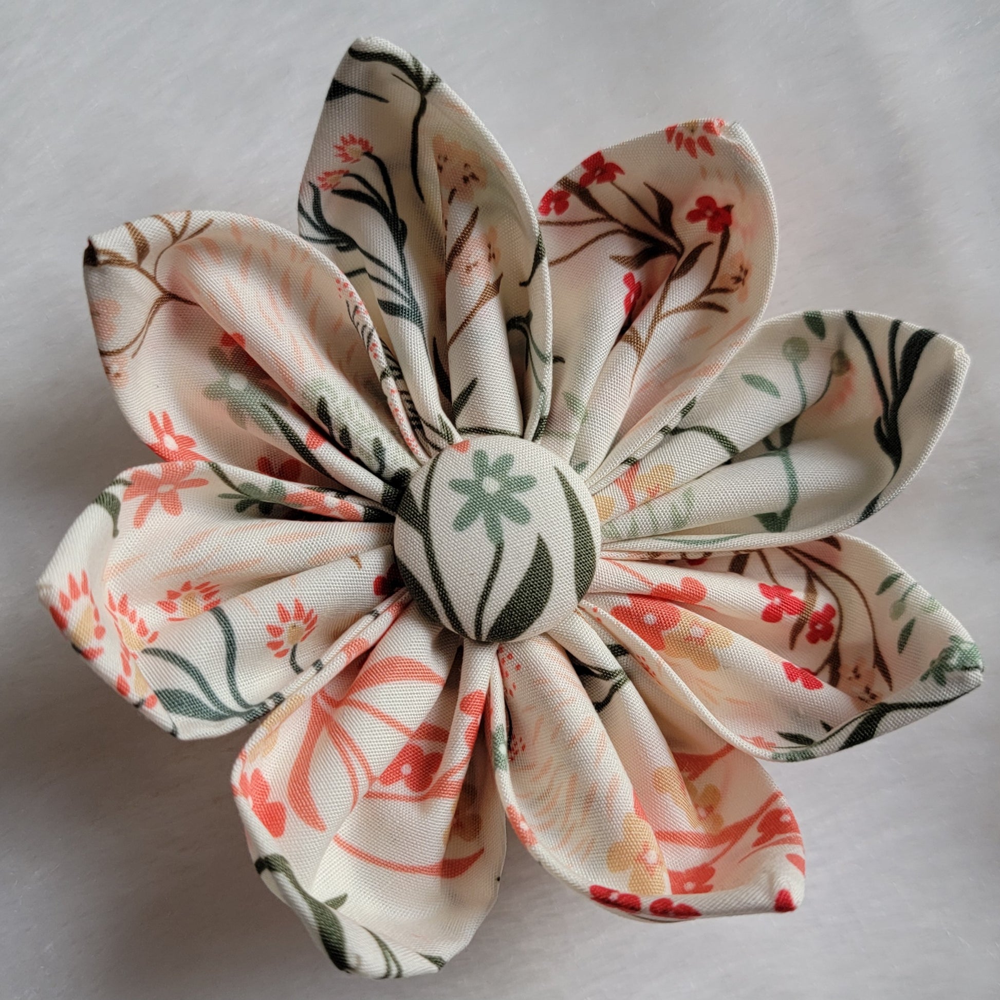 Fabric flower with eight petals and fabric covered button center, print is ivory with green and coral wildflowers.