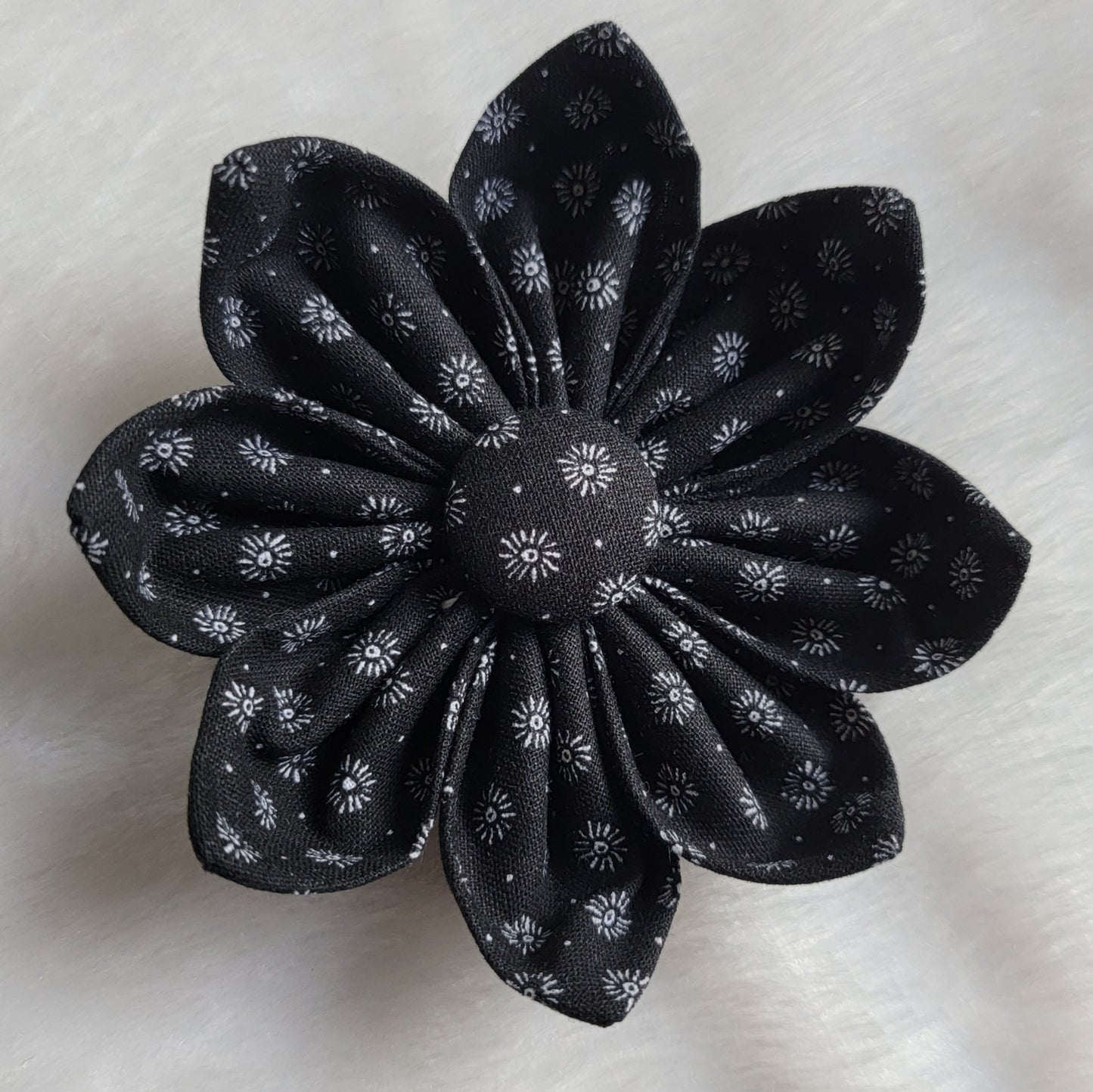 Fabric flower with eight petals and fabric covered button center, print is black with small white floral bursts.