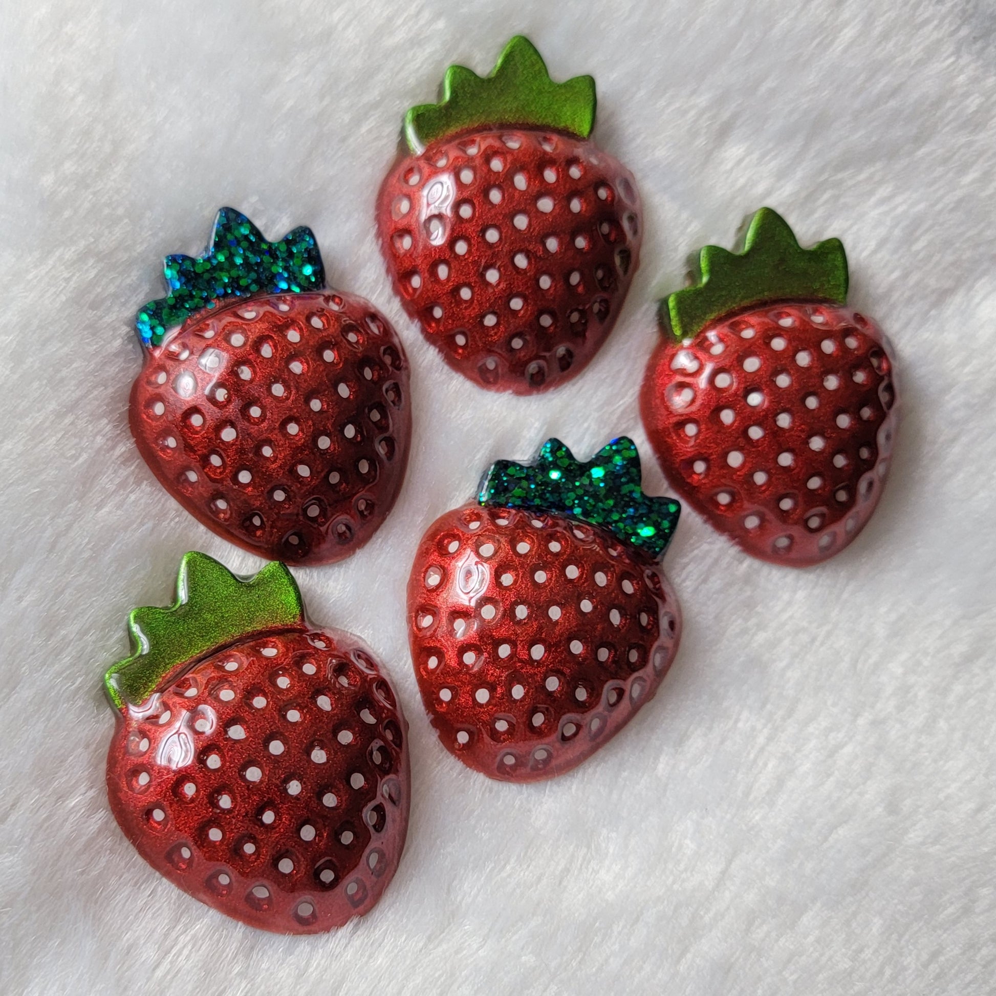 Five strawberry shaped epoxy resin pieces, bright metallic red pigment with hand painted white seeds and leaves in chrome green and green glitter.