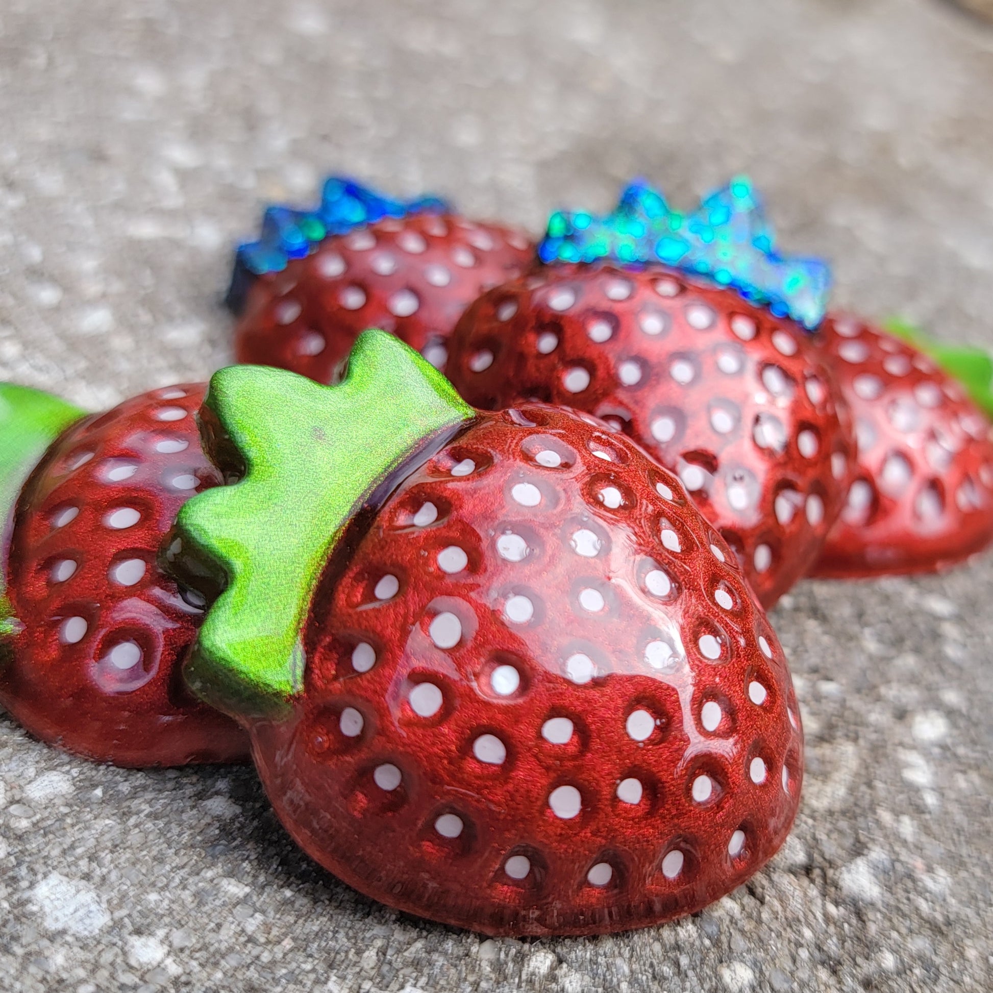 Five strawberry shaped epoxy resin pieces, bright metallic red pigment with hand painted white seeds and leaves in chrome green and green glitter.