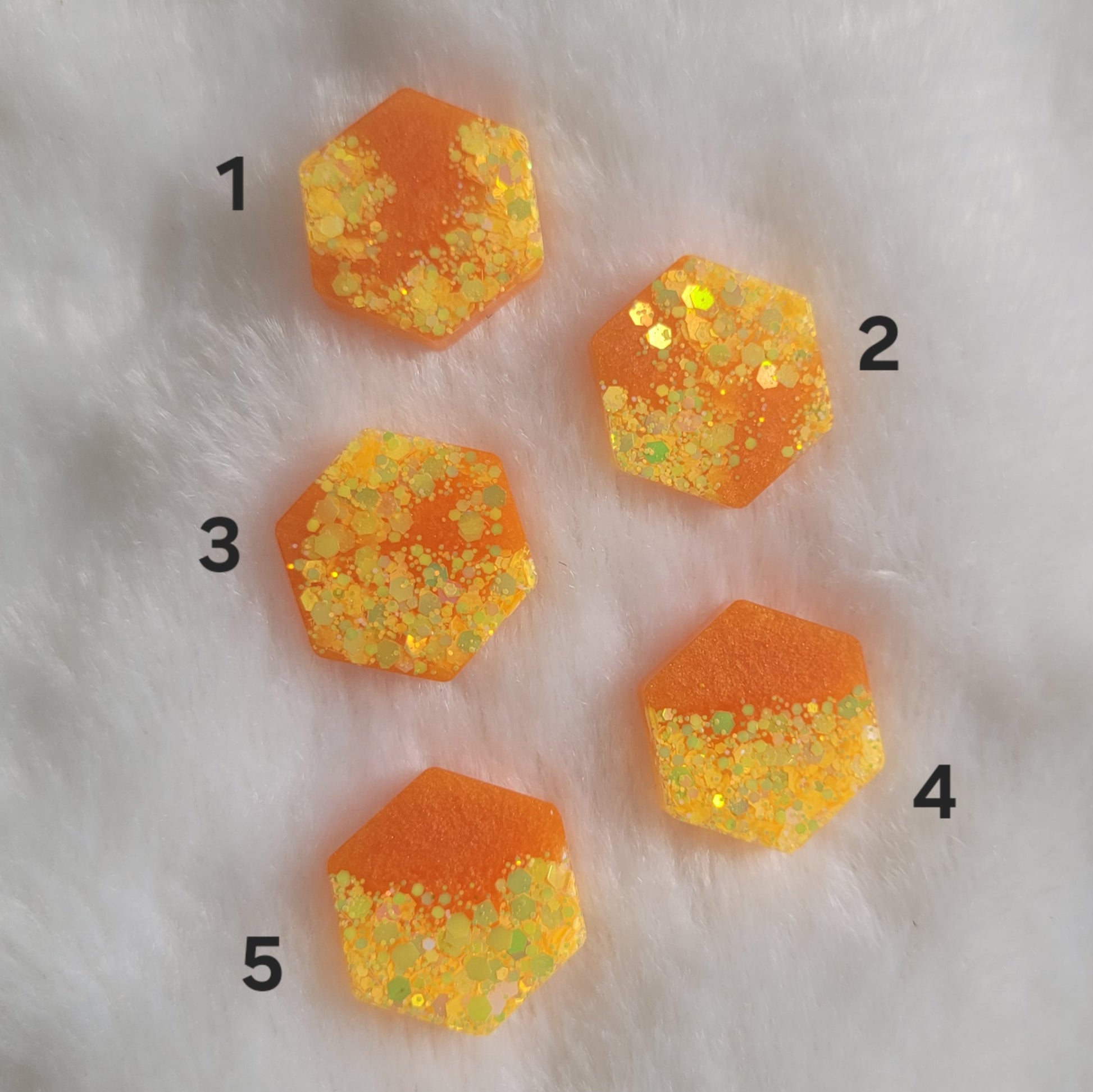 Five mini hexagon shaped epoxy resin pieces with orange pigment and yellow glitter.