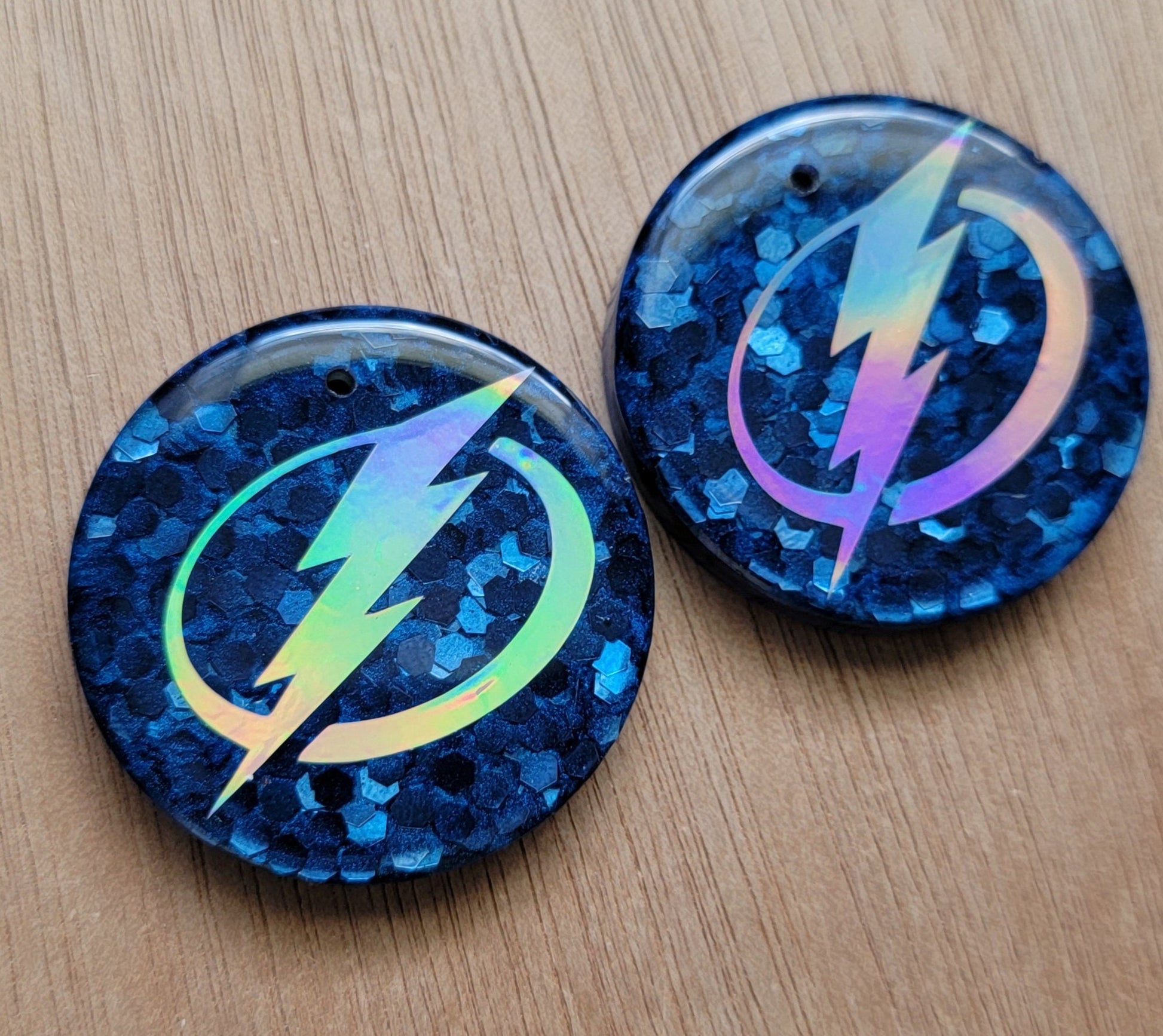 Two round epoxy resin pieces with navy blue base and silver holographic lightning logo design.