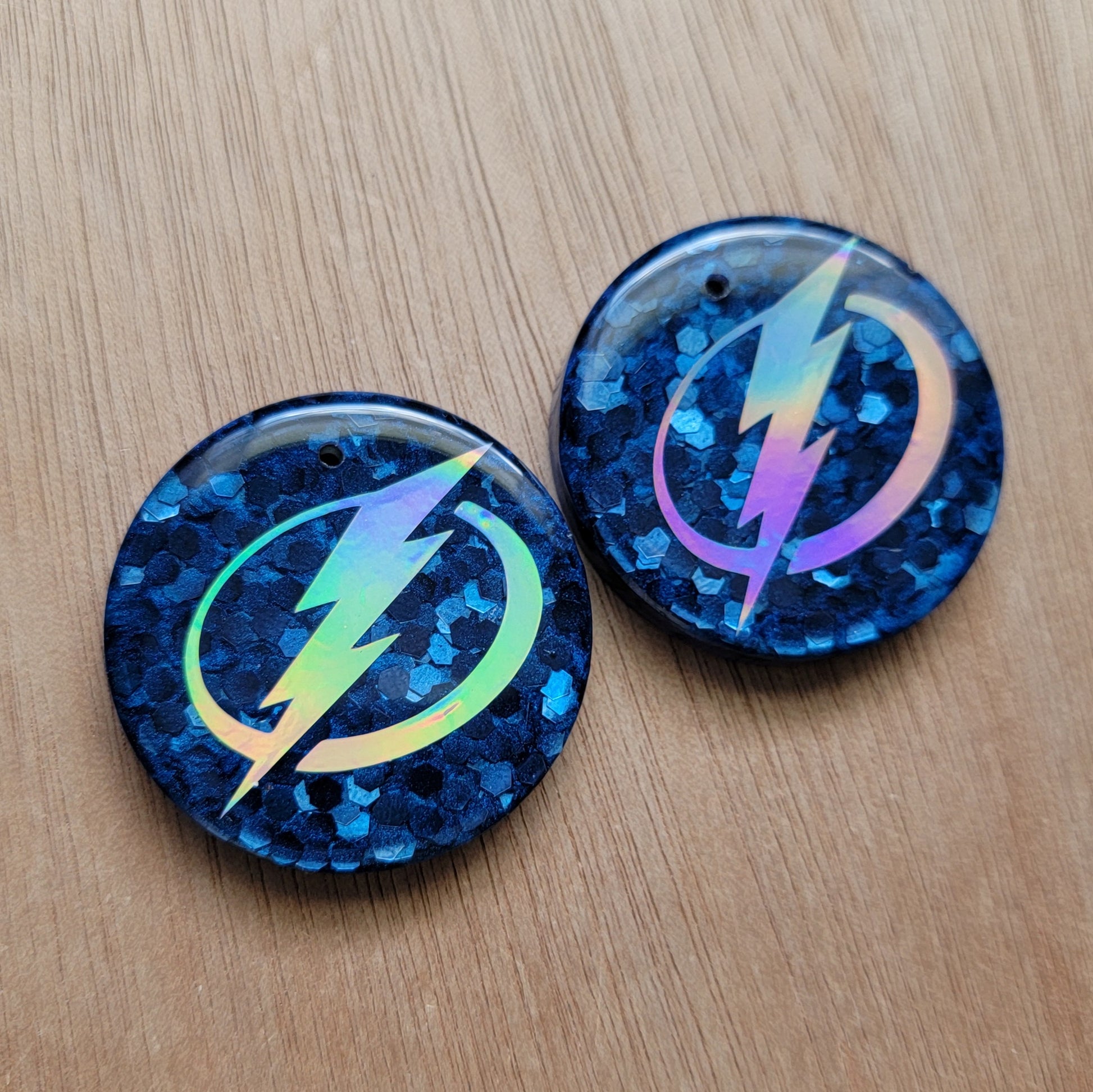 Customized round epoxy resin pieces with navy blue glitter base and holographic silver lighting logo design.