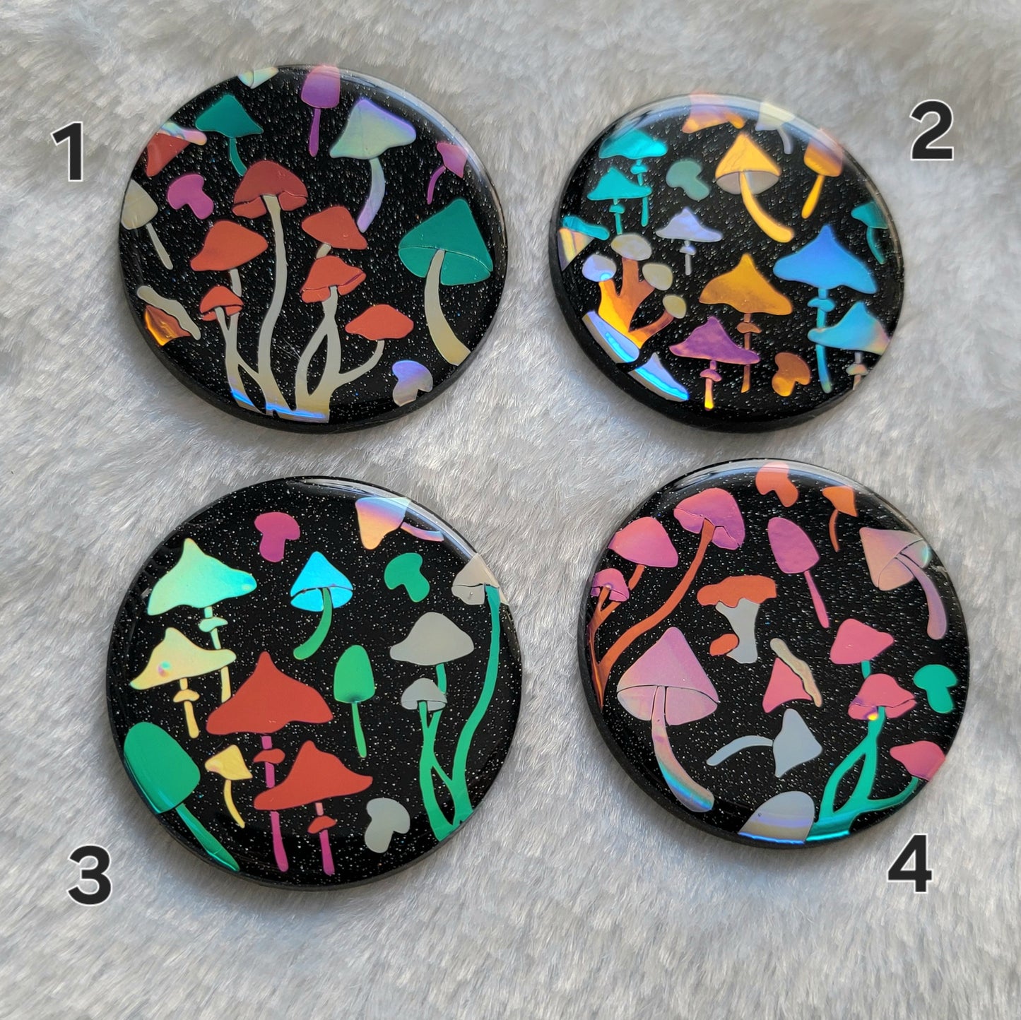 Four round sparkly black epoxy resin pieces with multicolored holographic mushrooms design.