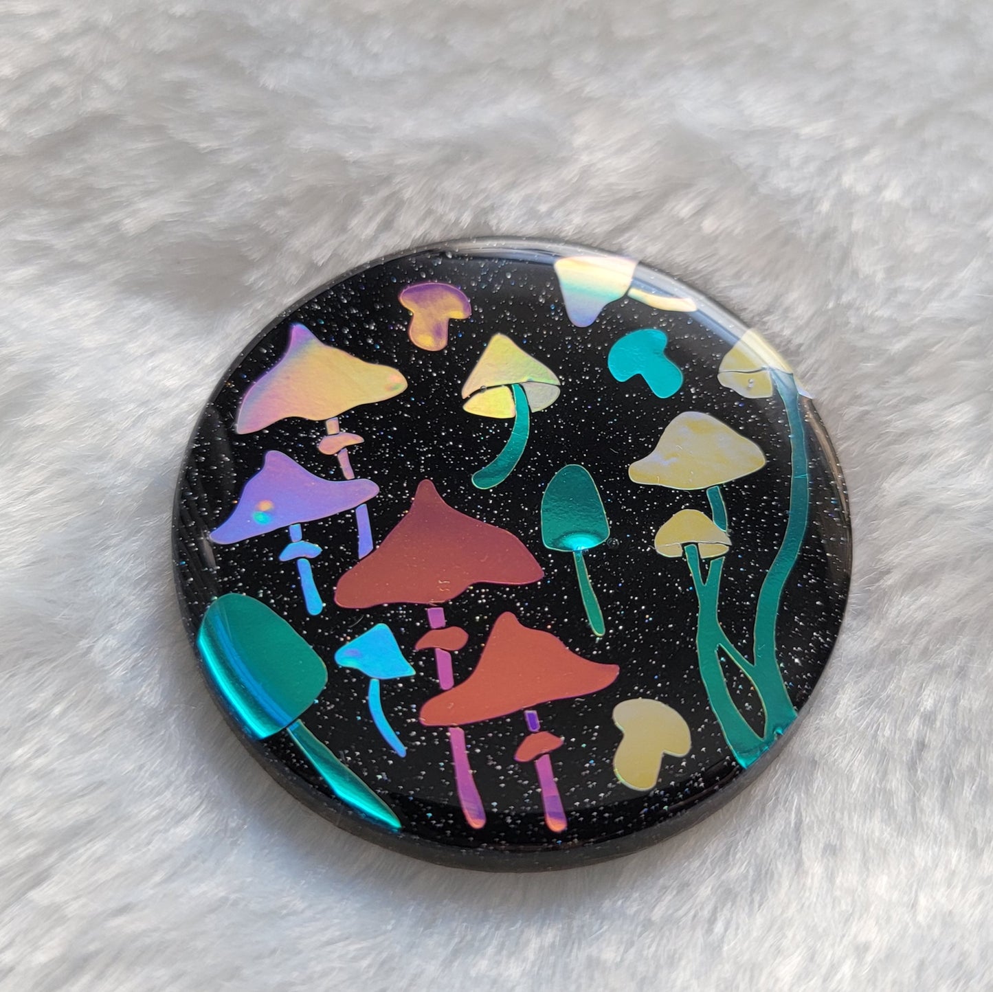 Round sparkly black epoxy resin piece with multicolored holographic mushrooms design.