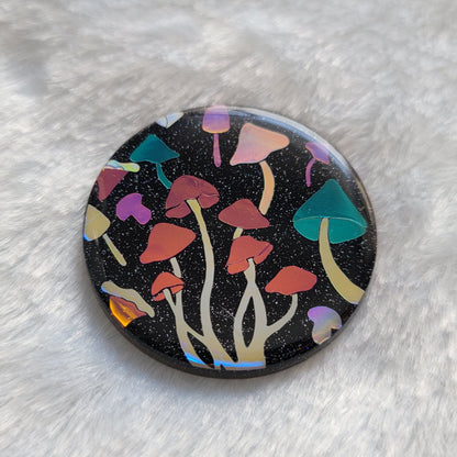 Round sparkly black epoxy resin piece with multicolored holographic mushrooms design.