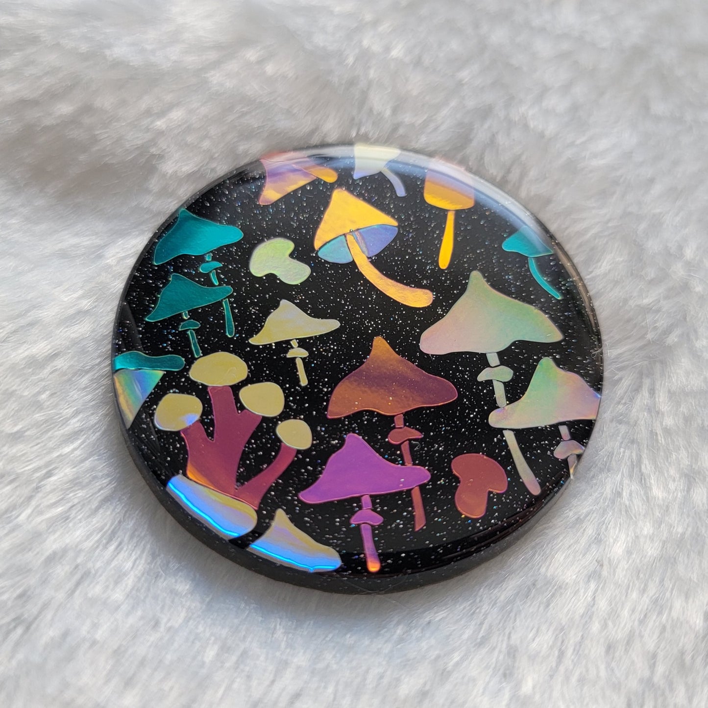 Round sparkly black epoxy resin piece with multicolored holographic mushrooms design.