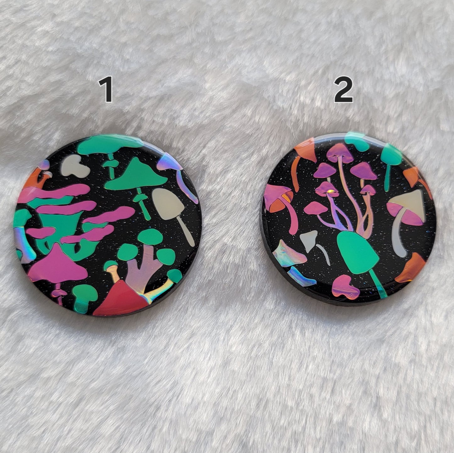 Two round sparkly black epoxy resin pieces with multicolored holographic mushrooms design.