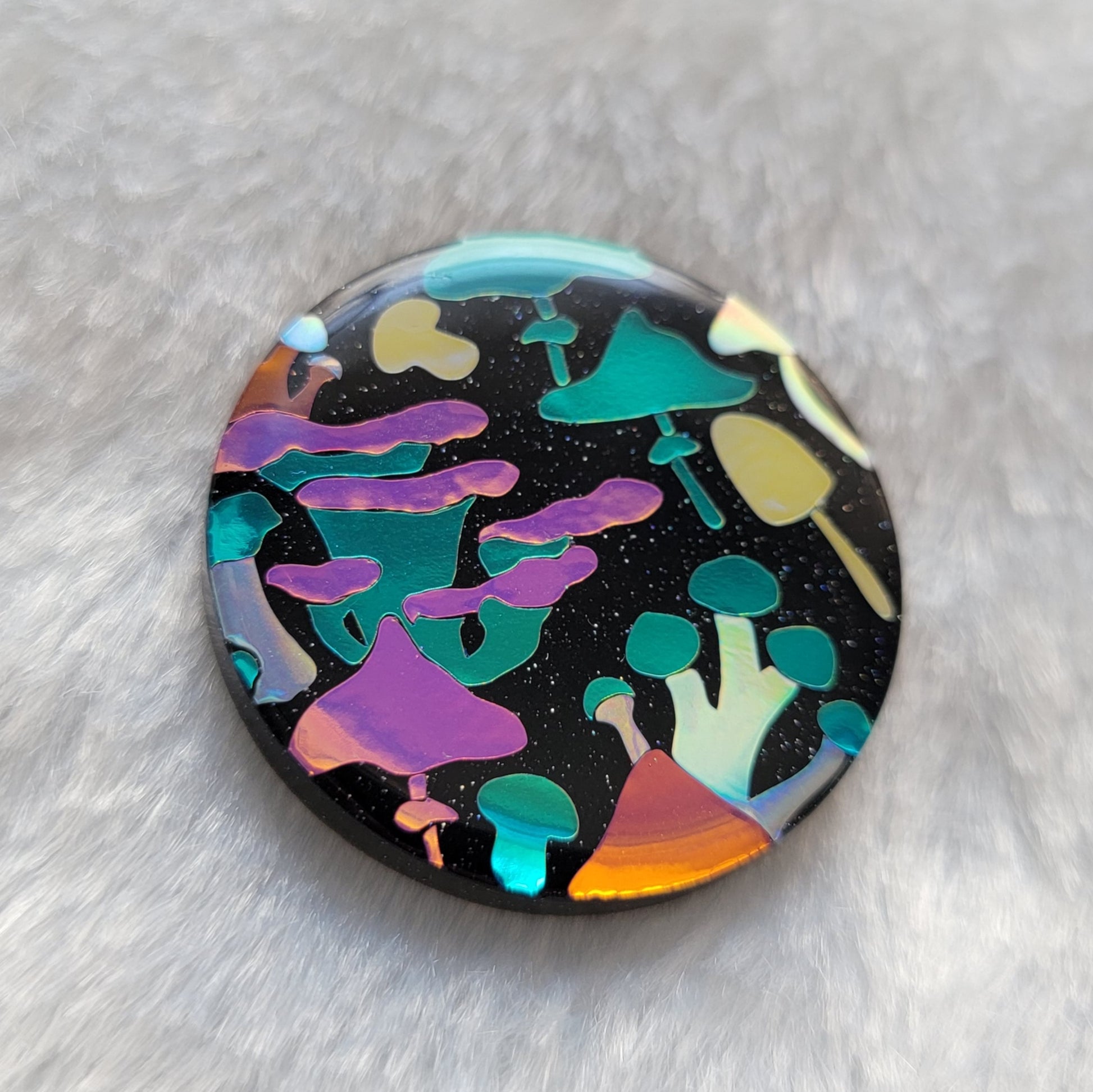 Round sparkly black epoxy resin piece with multicolored holographic mushrooms design.