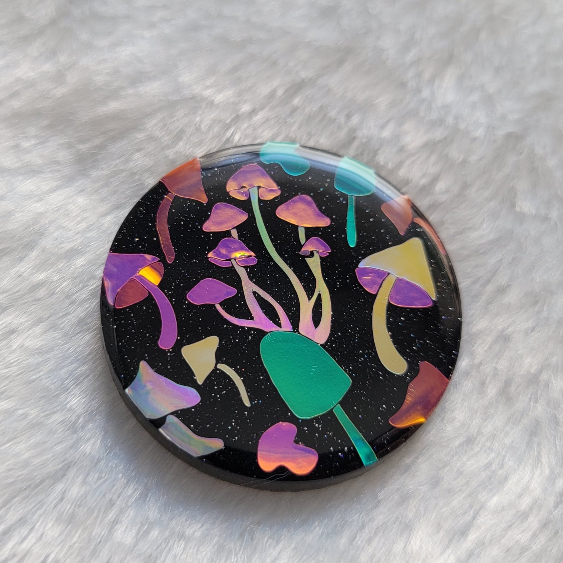 Round sparkly black epoxy resin piece with multicolored holographic mushrooms design.