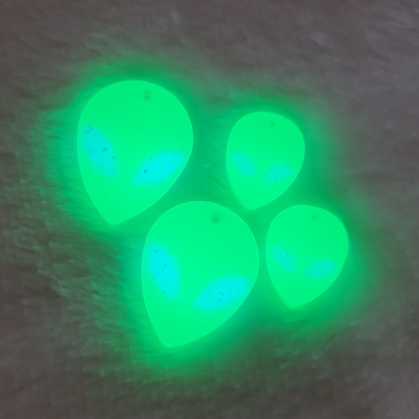 Bright green UV reactive alien head shaped epoxy resin pieces, shown glowing.