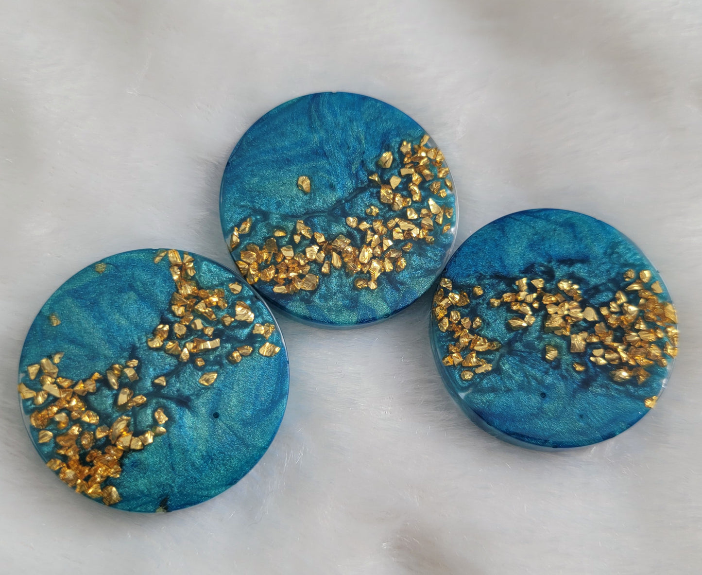 Three round epoxy resin pieces with mica swirls in shades of aqua blue and a stripe of gold glass glitter.