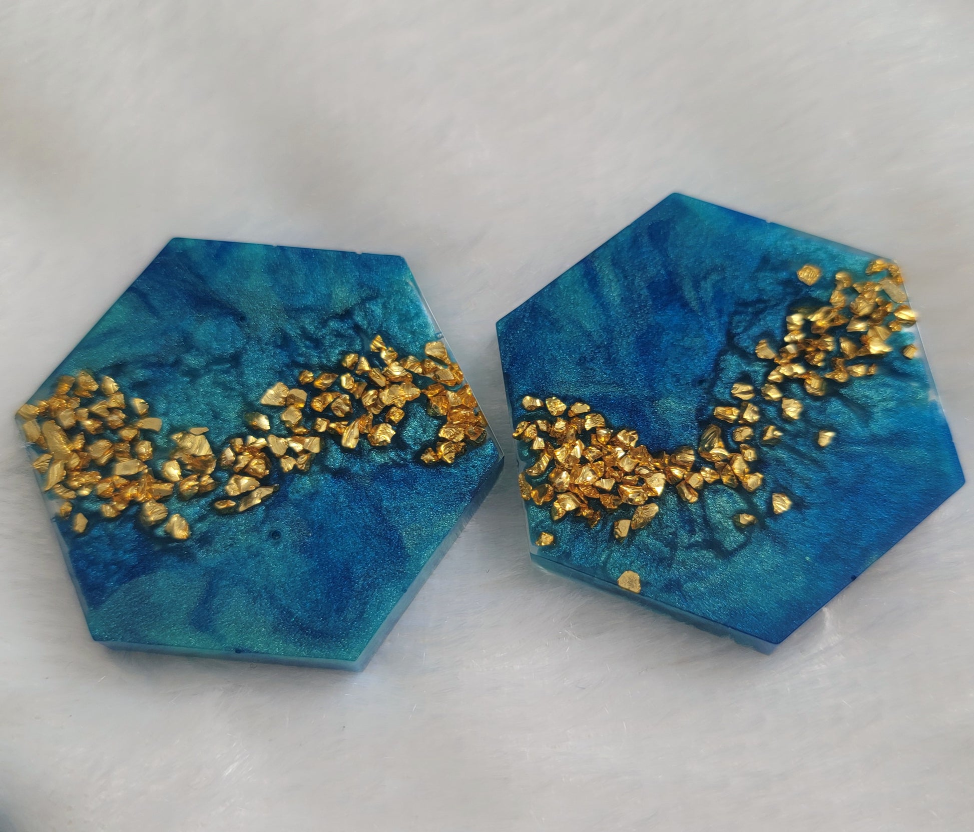 Two hexagon shaped epoxy resin pieces with mica swirls in shades of aqua blue and a stripe of gold glass glitter.