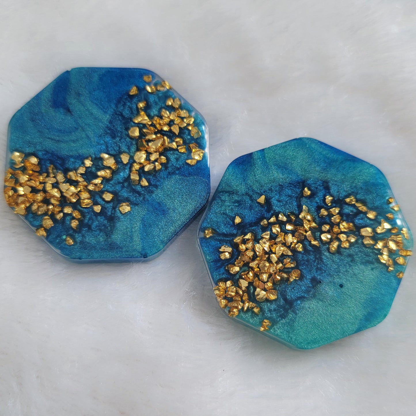 Two octagon shaped epoxy resin pieces with mica swirls in shades of aqua blue and a stripe of gold glass glitter.