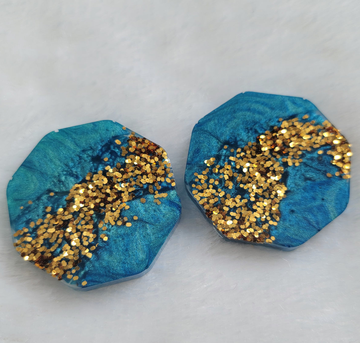 Two octagon shaped epoxy resin pieces with mica swirls in shades of aqua blue and a stripe of gold glitter.