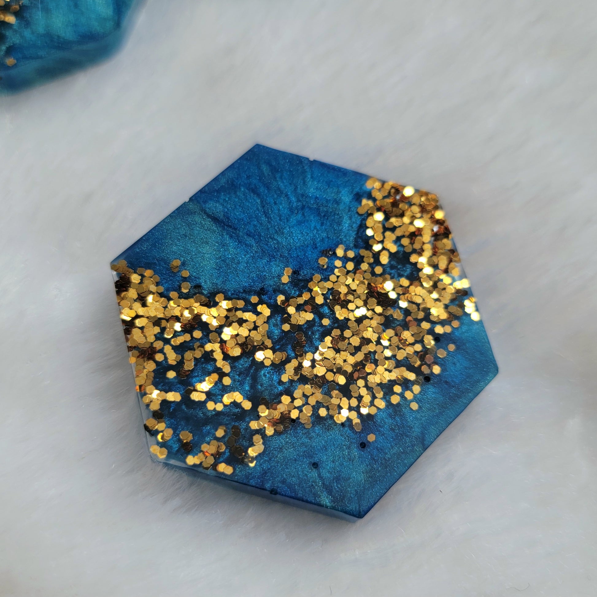 Hexagon shaped epoxy resin piece with mica swirls in shades of aqua blue and a stripe of gold glitter.