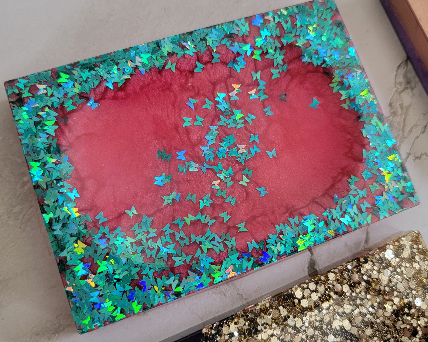 Square epoxy resin soap dish with vibrant magenta mica pigment and holographic blue butterfly glitter.