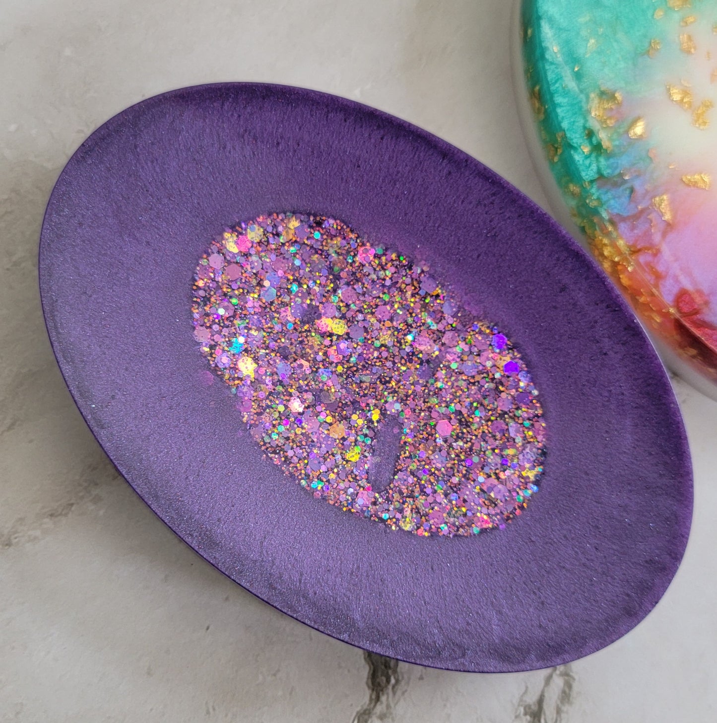 Round epoxy resin soap dish with muted purple border and sparkly purple glitter center.