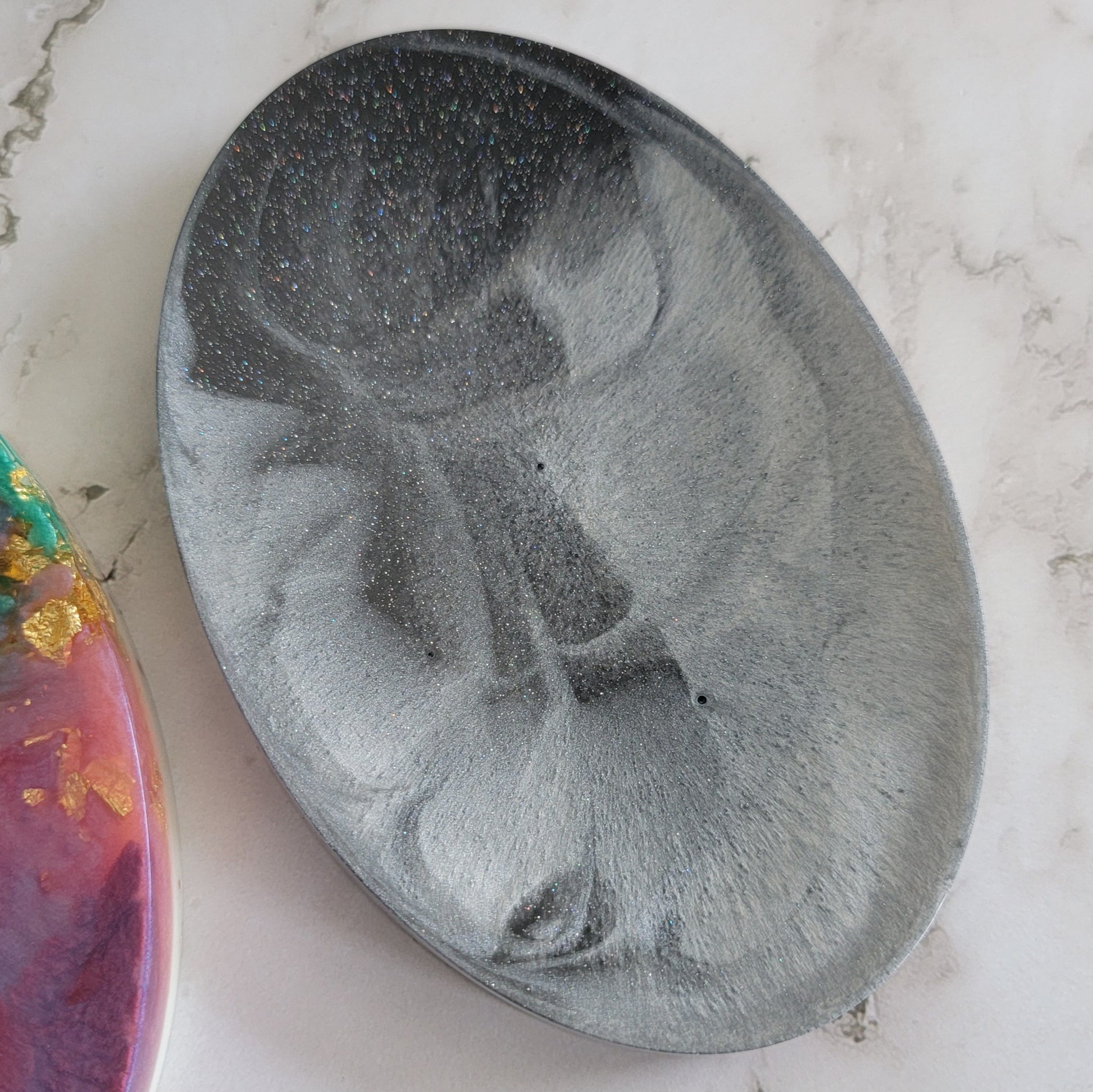 Round epoxy resin soap dish with black and silver swirls and holographic silver micro glitter.