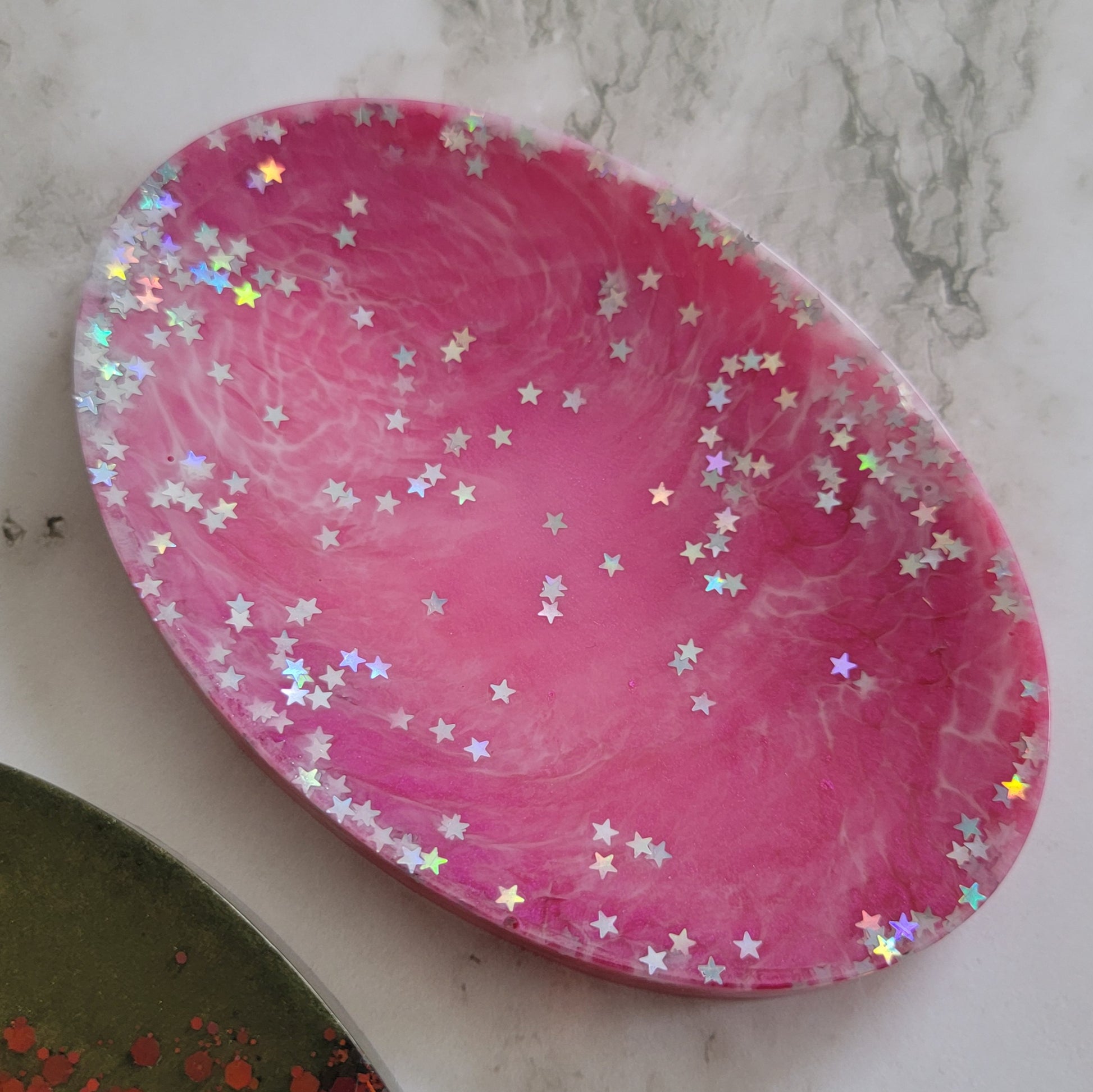 Round epoxy resin soap dish with dark pink and white swirls and holographic silver star glitter.