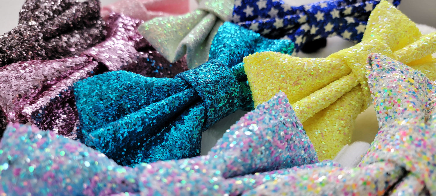 Several glitter bows, colors shown include: pewter, lilac, aqua blue, ice blue, deep blue with stars, bright yellow, and confetti.