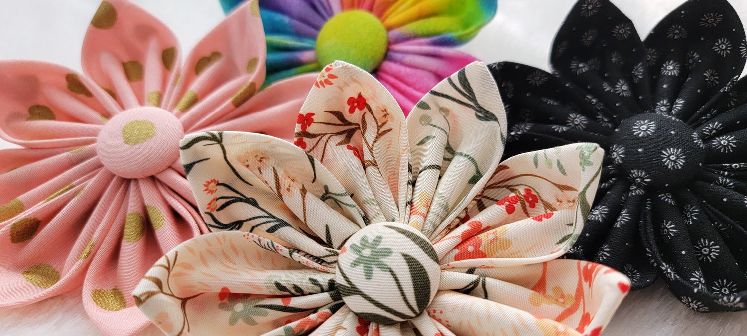 Four fabric flowers, styles shown include: floral print on ivory, black with white starburst, pink with gold dots, and rainbow watercolor swirls.