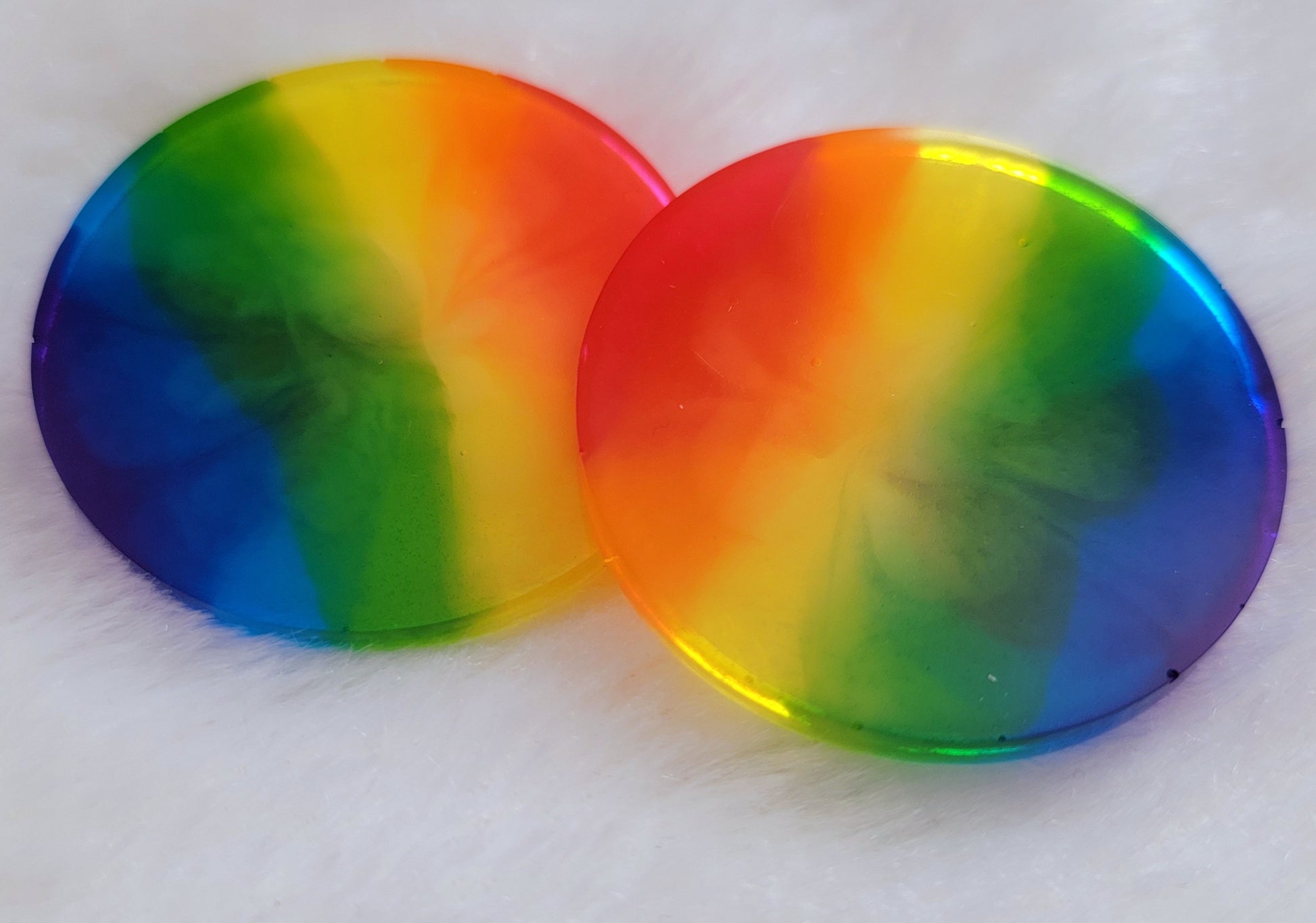 Two round epoxy resin pieces with subtle bloom effect in translucent rainbow stripes.