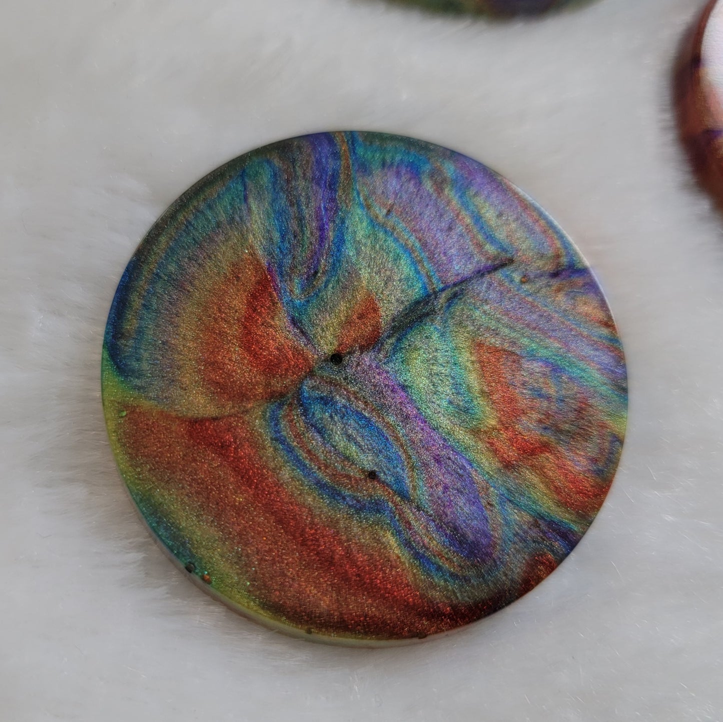 Round epoxy resin piece with colorful shimmering psychedelic swirls.