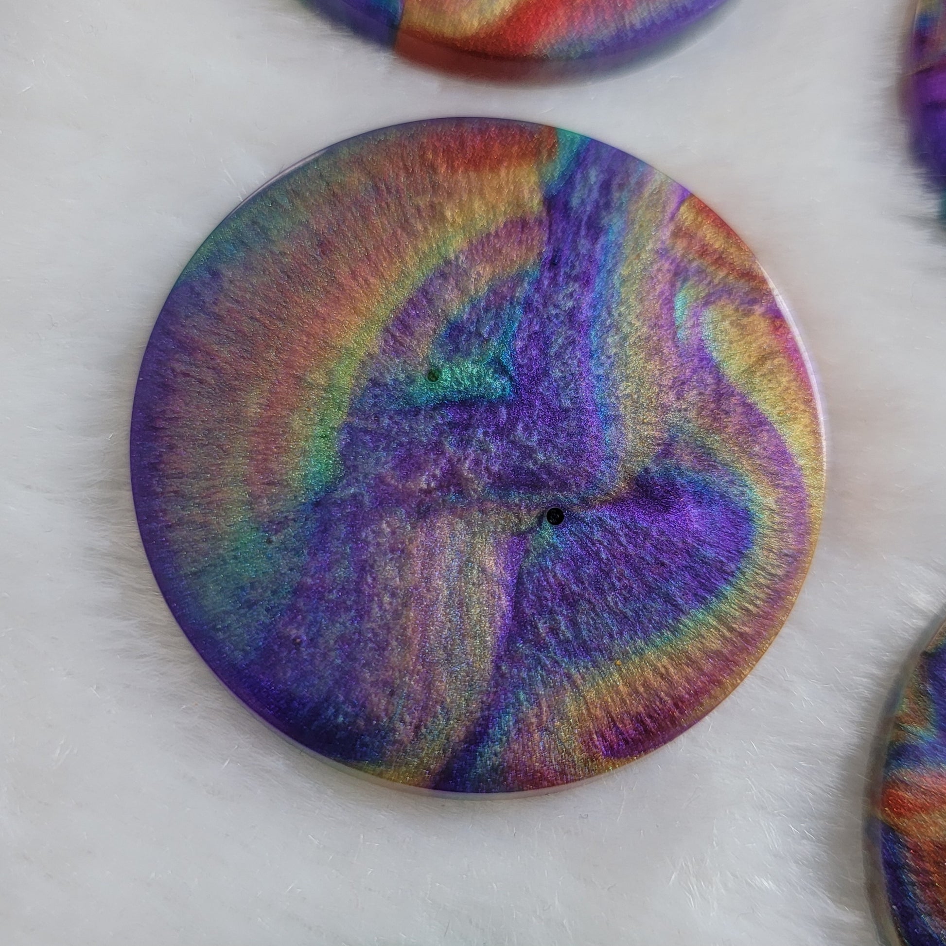 Round epoxy resin piece with colorful shimmering psychedelic swirls.