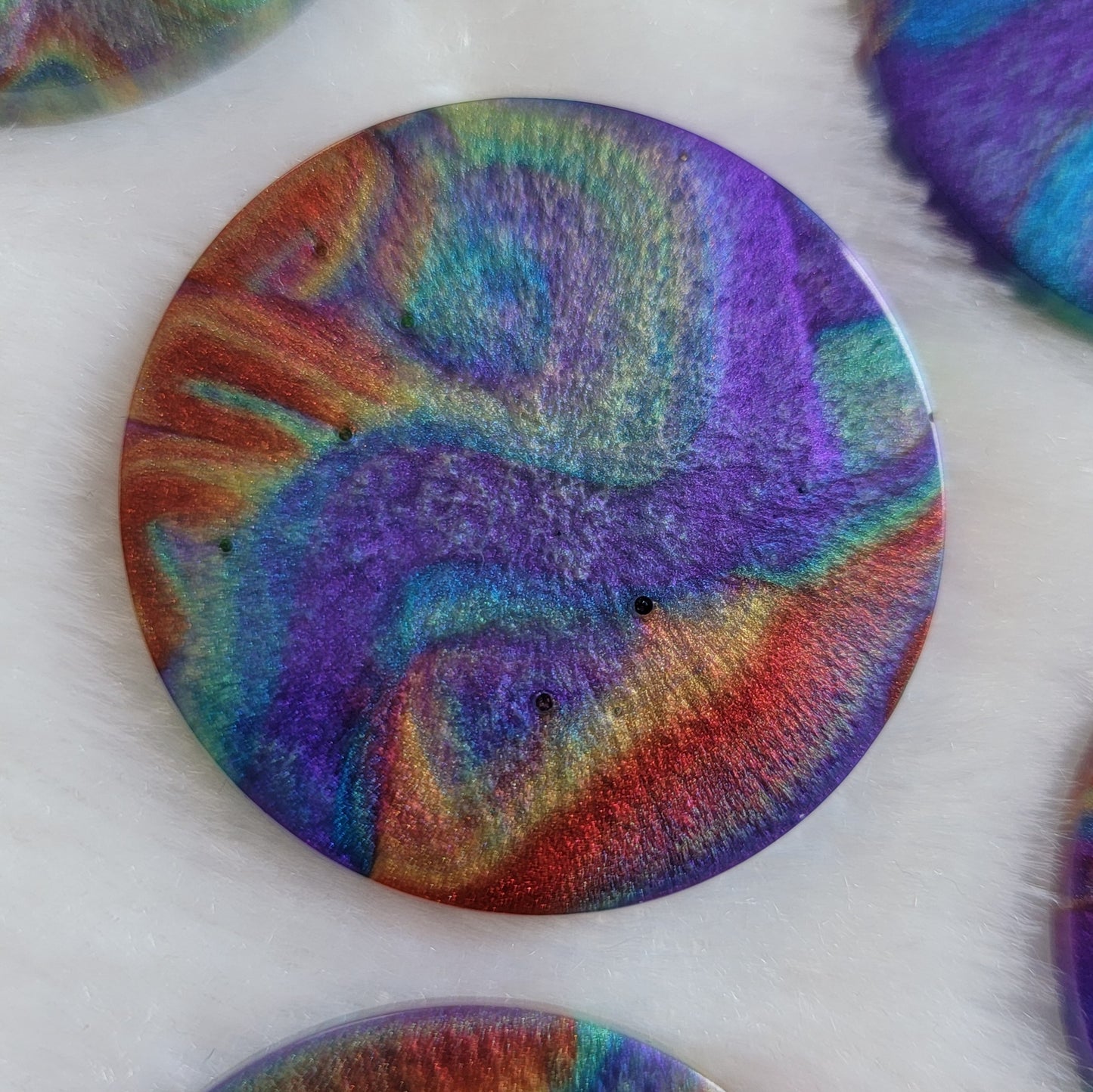 Round epoxy resin piece with colorful shimmering psychedelic swirls.