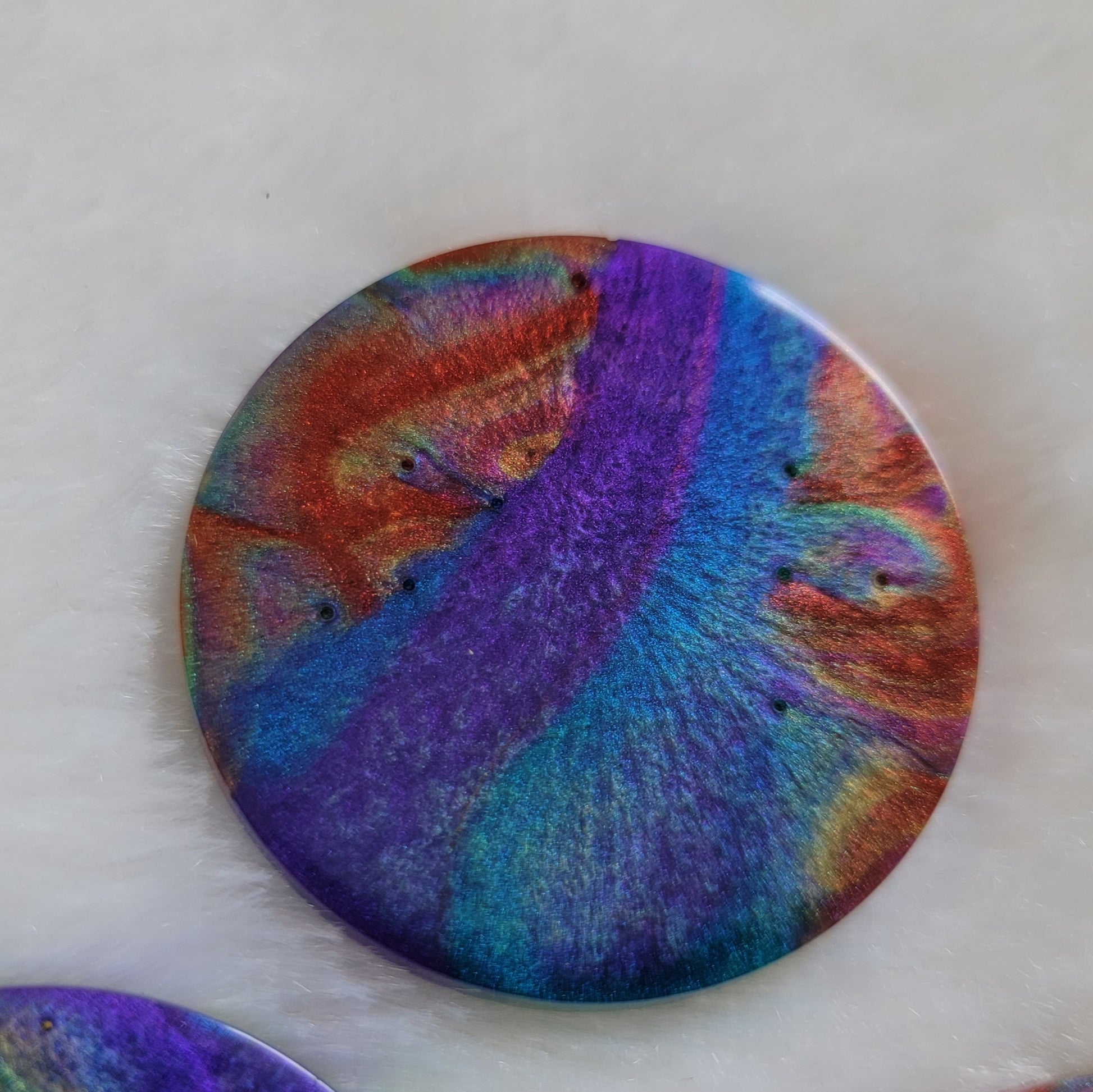 Round epoxy resin piece with colorful shimmering psychedelic swirls.