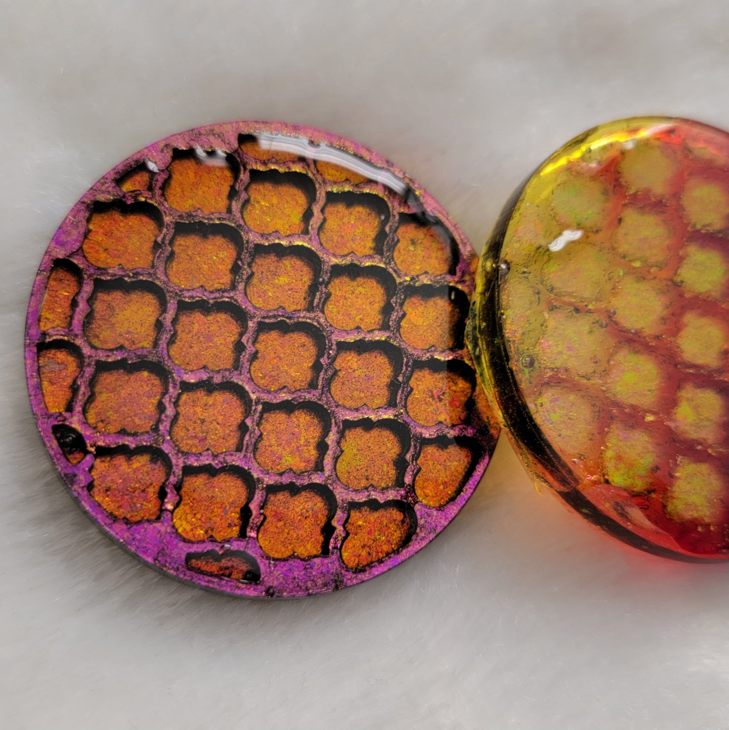 Two round epoxy resin pieces with geometric tile pattern and pink/gold iridescent pigment, one opaque one translucent.