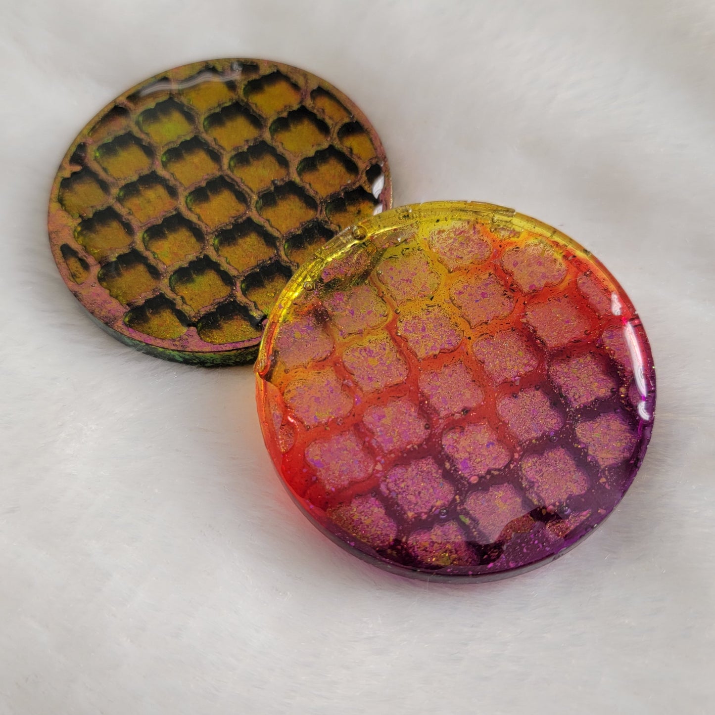 Two round epoxy resin pieces with geometric tile pattern and pink/gold iridescent pigment, one opaque one translucent.