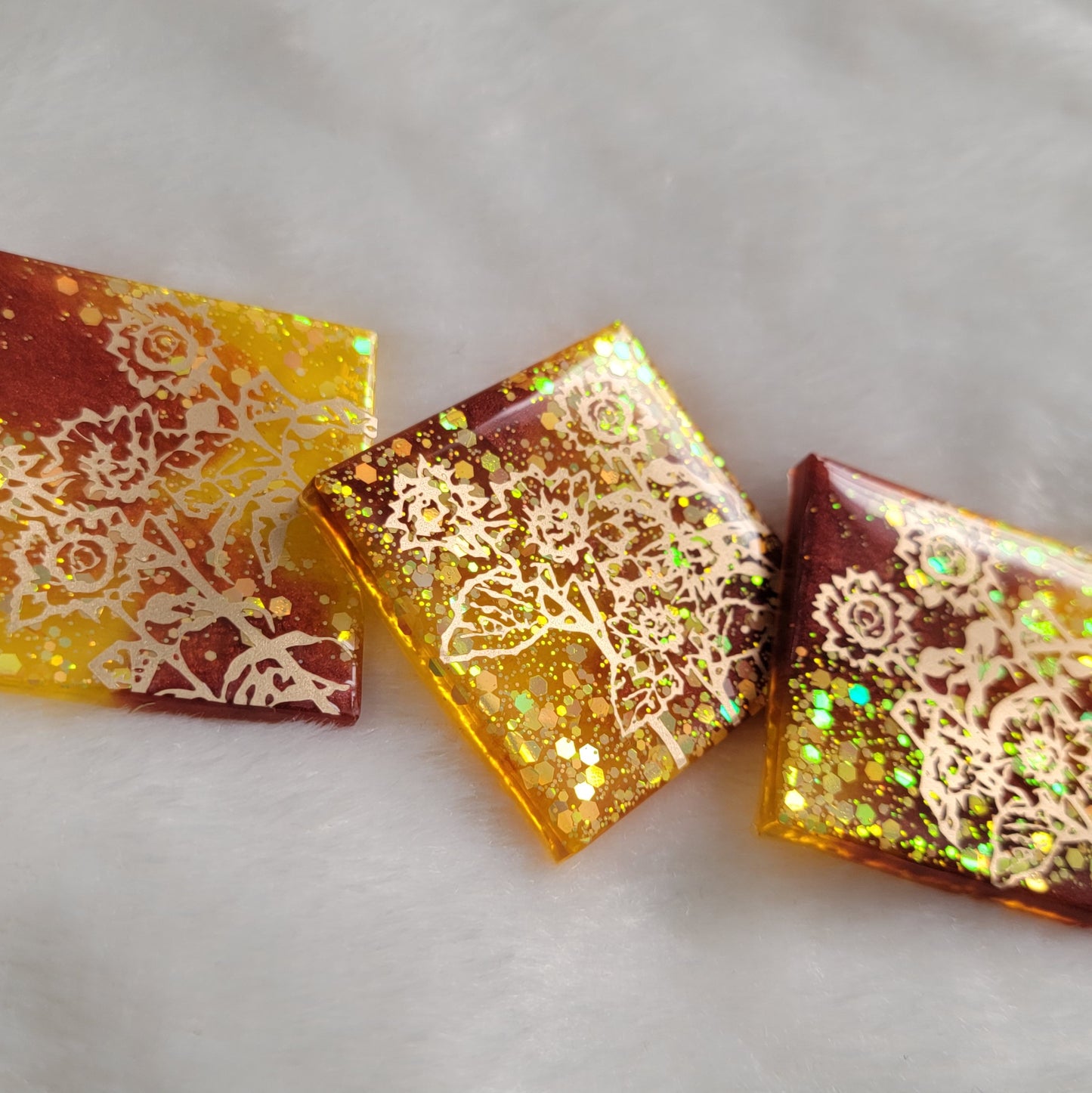 Three square epoxy resin pieces, yellow glitter and rust mica pigment swirls with gold vinyl sunflower design.