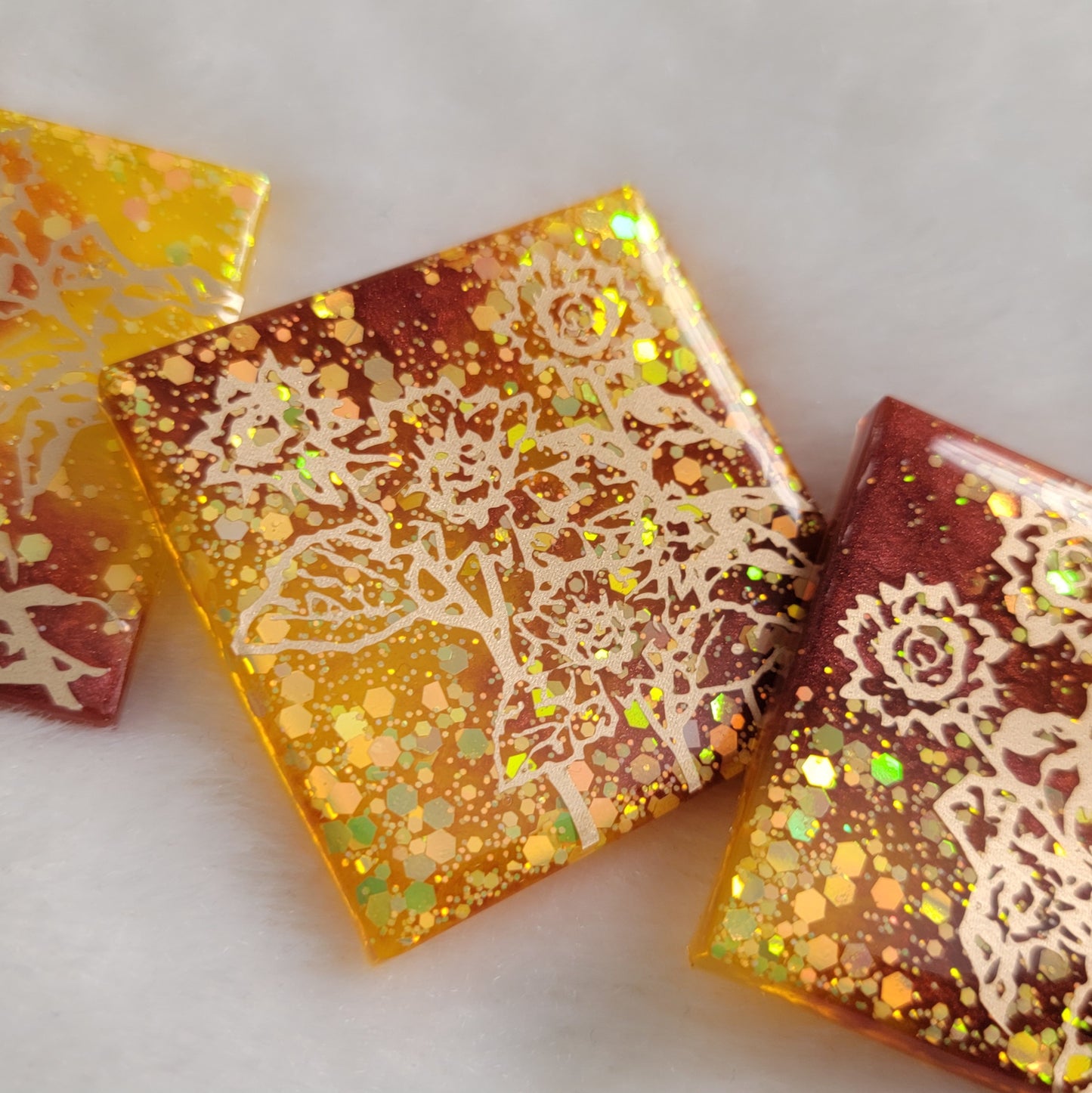 Three square epoxy resin pieces, yellow glitter and rust mica pigment swirls with gold vinyl sunflower design.