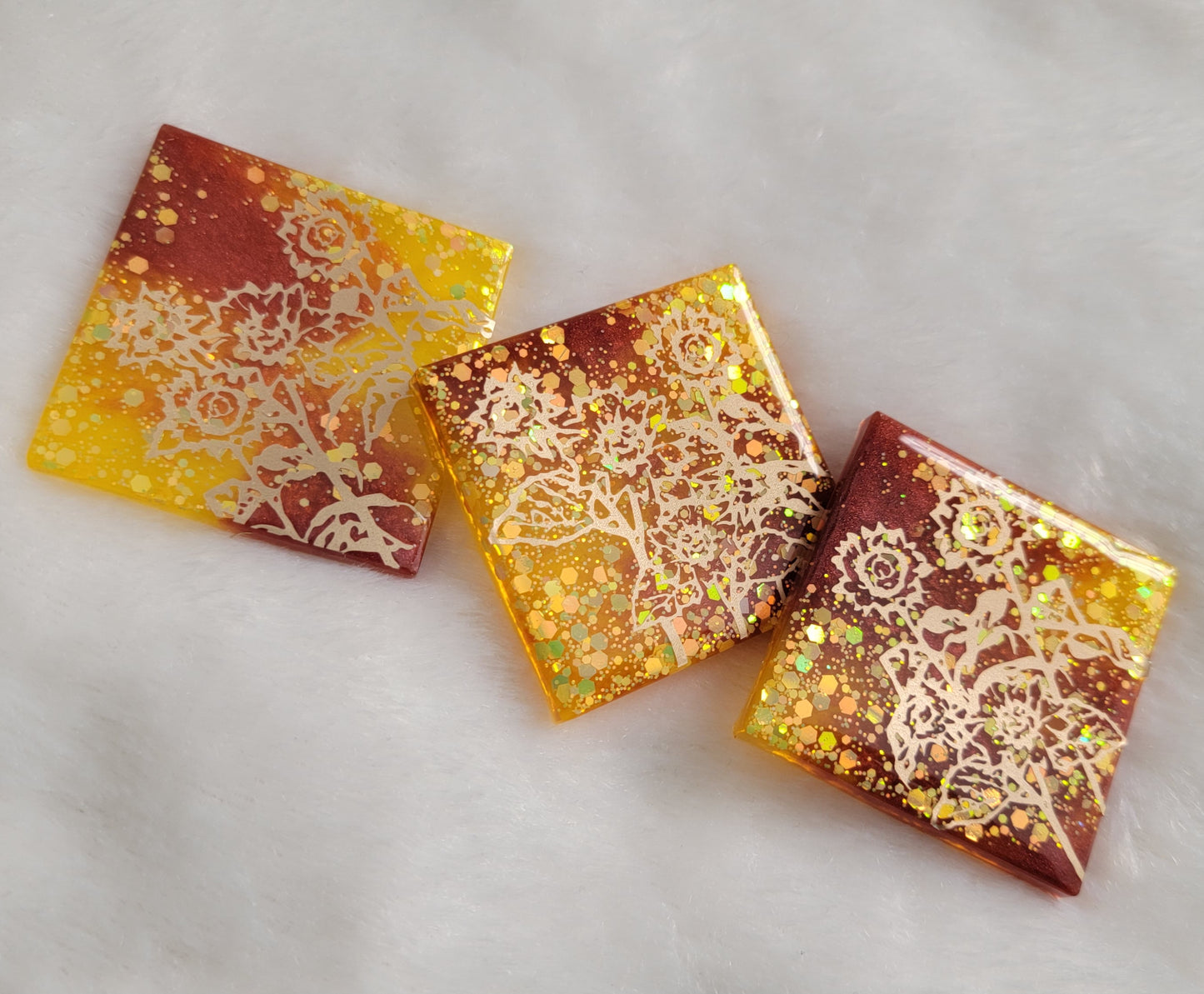 Three square epoxy resin pieces, yellow glitter and rust mica pigment swirls with gold vinyl sunflower design.