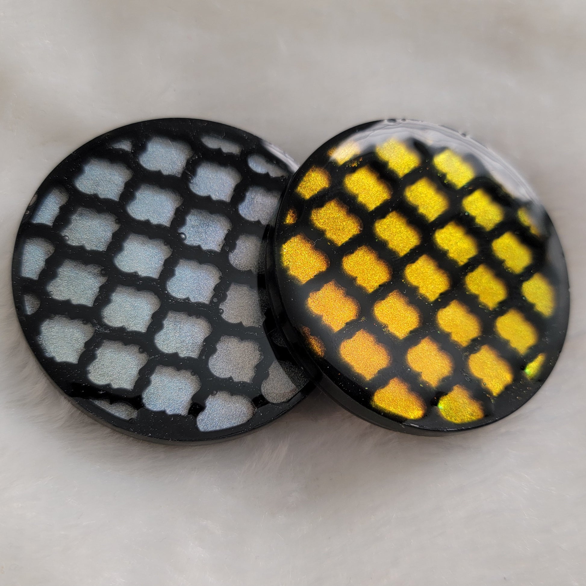 Two round epoxy resin pieces with black lattice pattern in iridescent gold and silver.