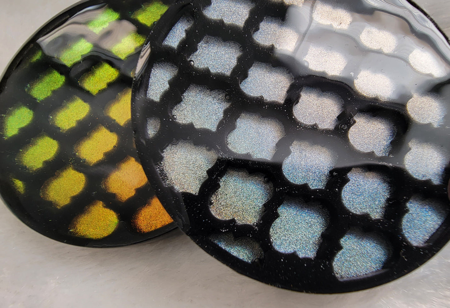 Two round epoxy resin pieces with black lattice pattern in iridescent gold and silver.