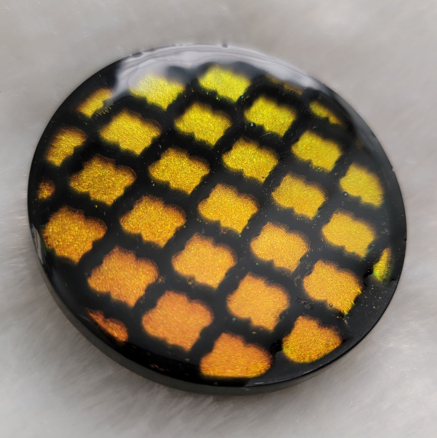 Round epoxy resin piece with black and iridescent gold lattice pattern.