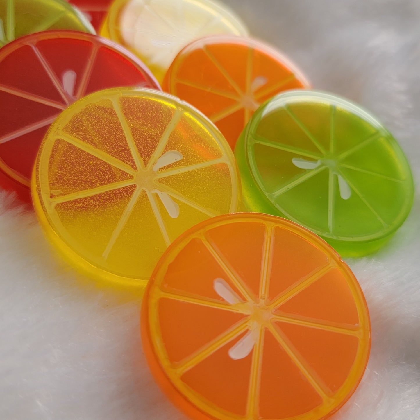 Eight round epoxy resin pieces in vibrant translucent colors with painted details to look like citrus slices.