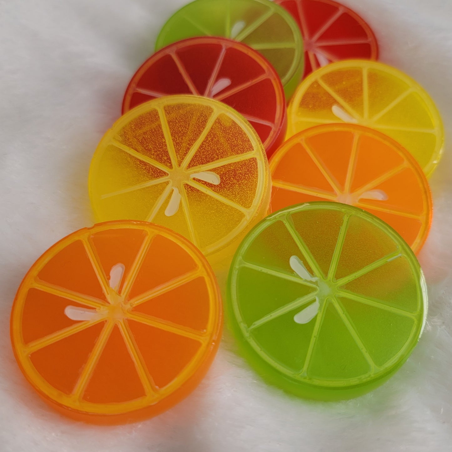 Eight round epoxy resin pieces in vibrant translucent colors with painted details to look like citrus slices.