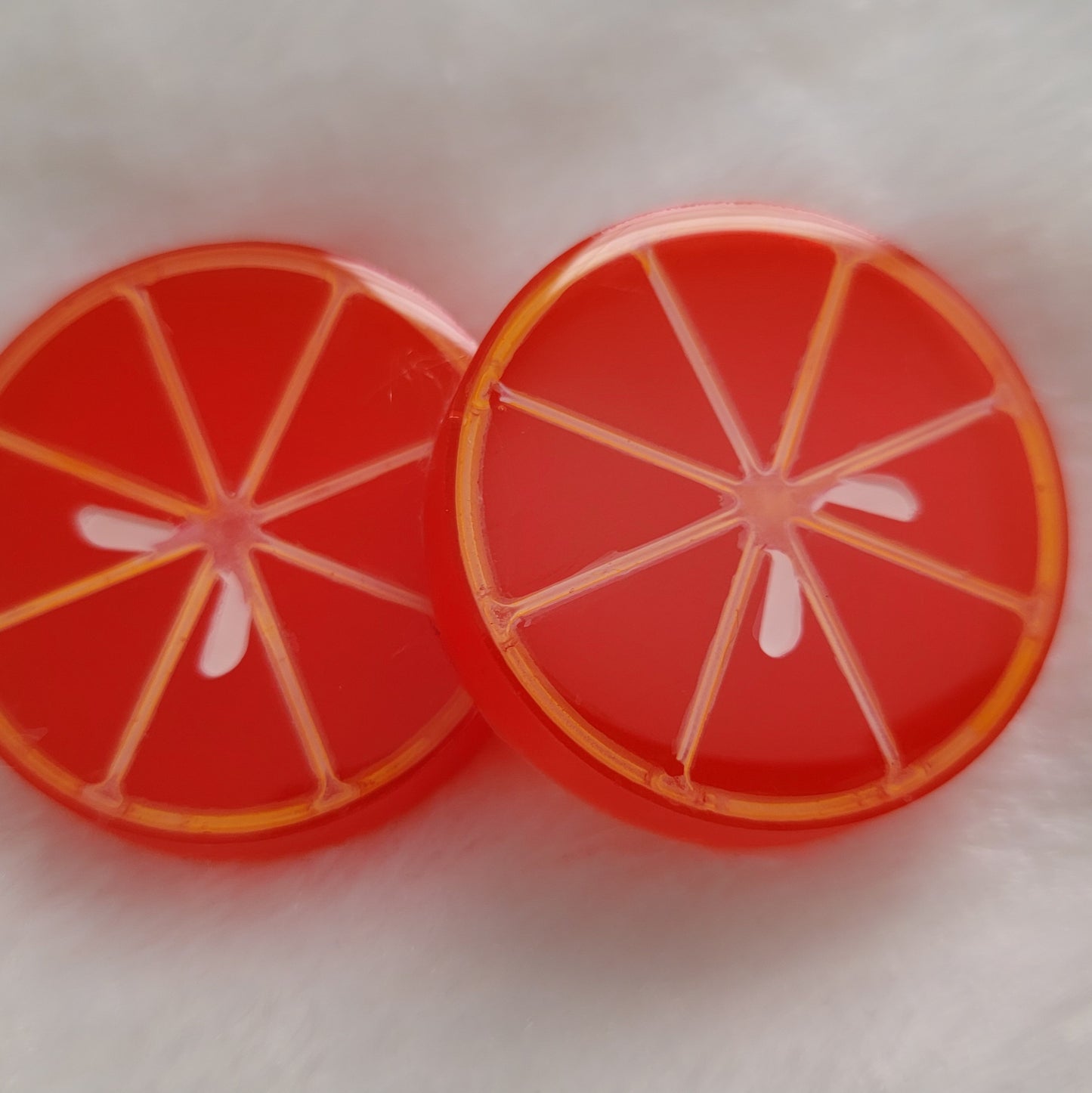 Two round epoxy resin pieces, bright red-orange translucent color with details to look like blood orange slice.