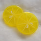 Two round epoxy resin pieces, bright yellow translucent color with details to look like lemon slice.