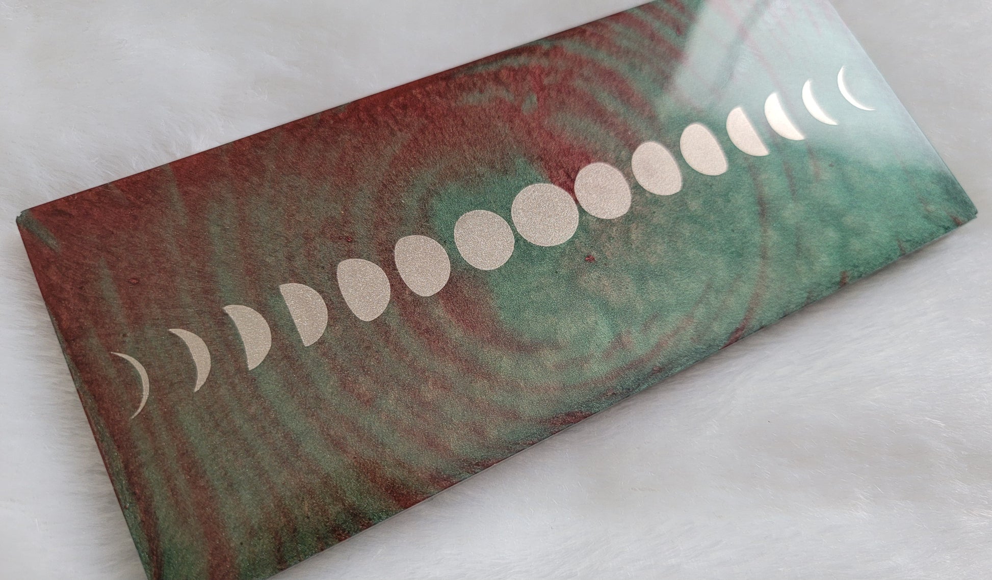 Rectangular epoxy resin piece with metallic moon phases motif on earthy green and rust swirled base.