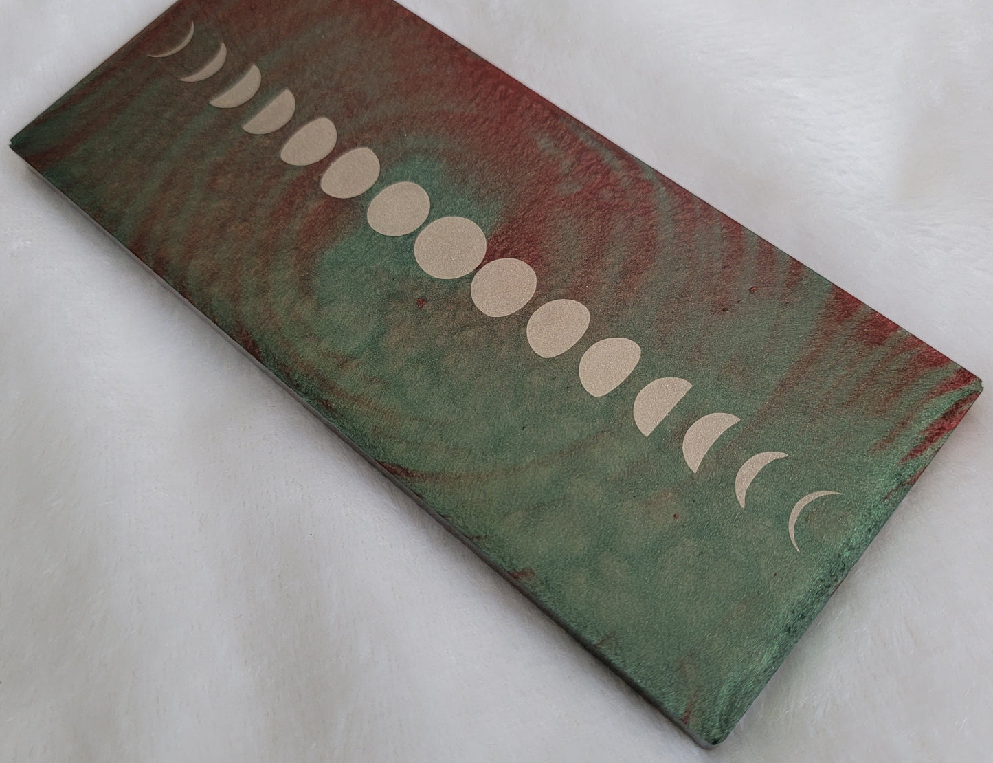 Rectangular epoxy resin piece with metallic moon phases motif on earthy green and rust swirled base.