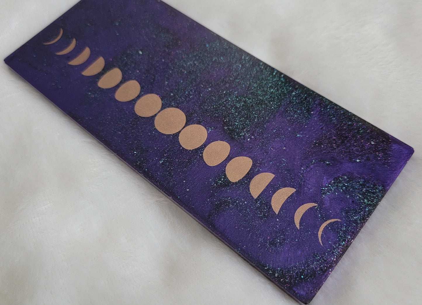 Rectangular epoxy resin piece with metallic moon phases motif on deep purple and iridescent green sparkle base.