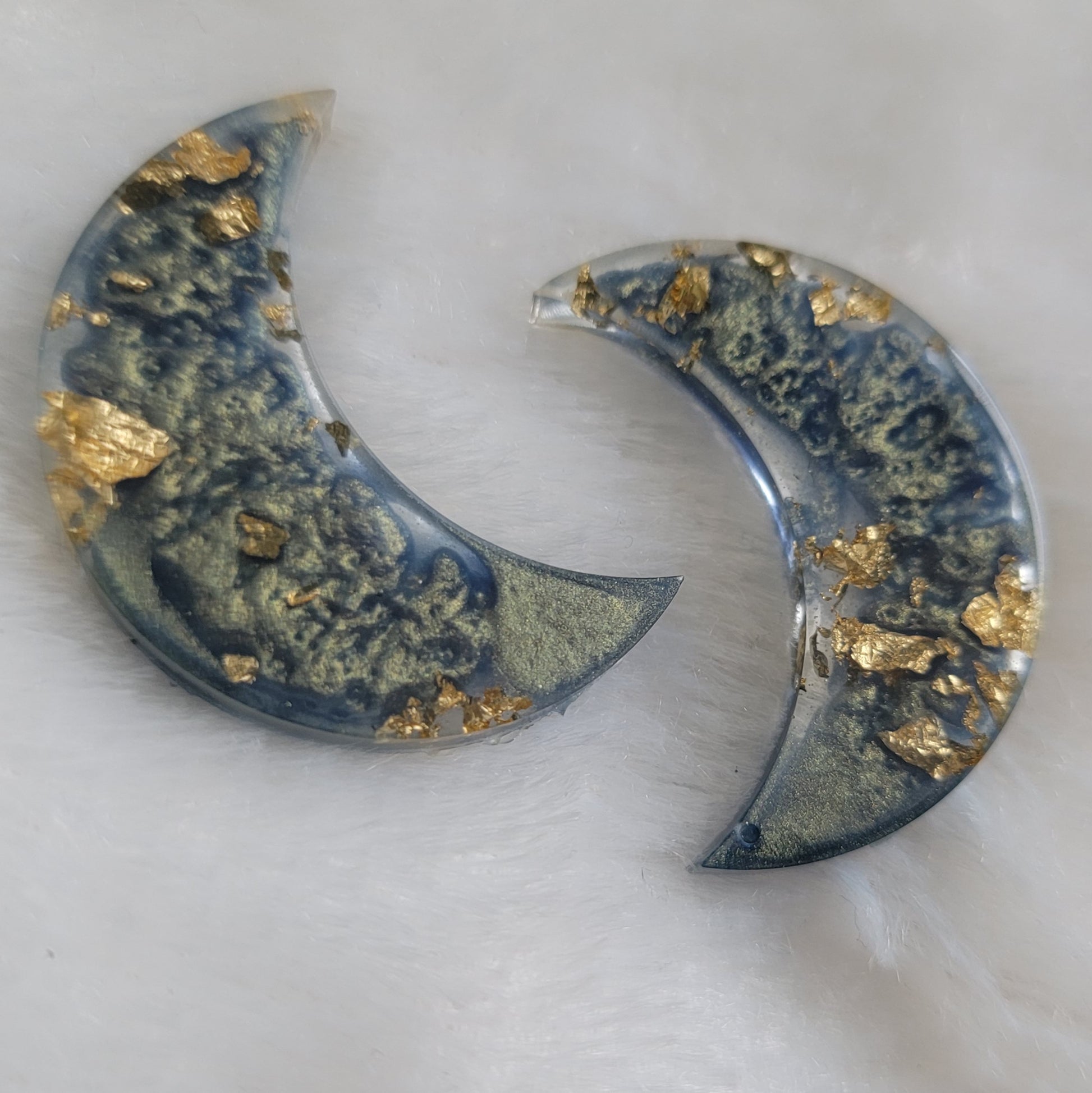 Two crescent moon shaped epoxy resin pieces with misty blue swirls and gold foil flakes.